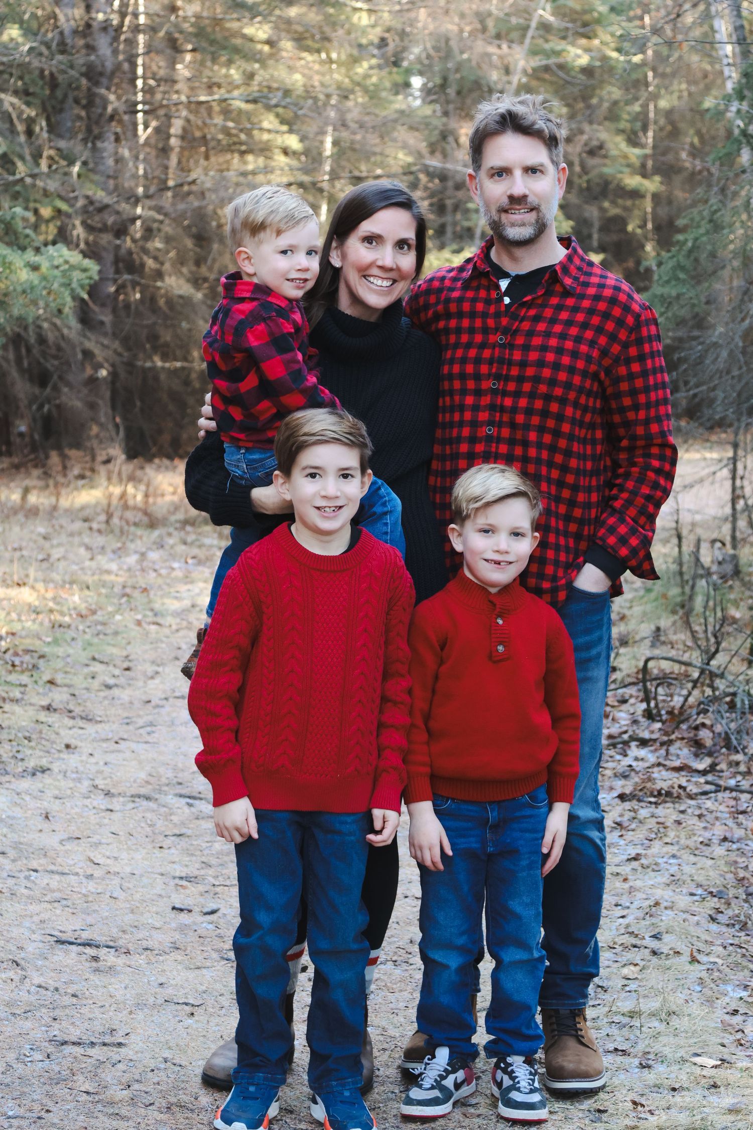Family of five in red and black plaid poses on forest path with three young boys.