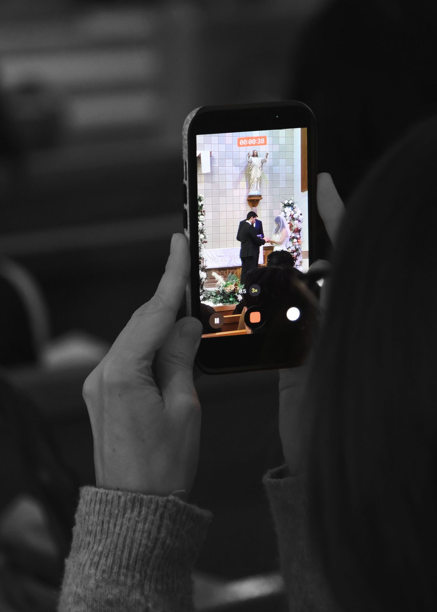 Guest recording wedding ceremony on smartphone in black and white photo at church.
