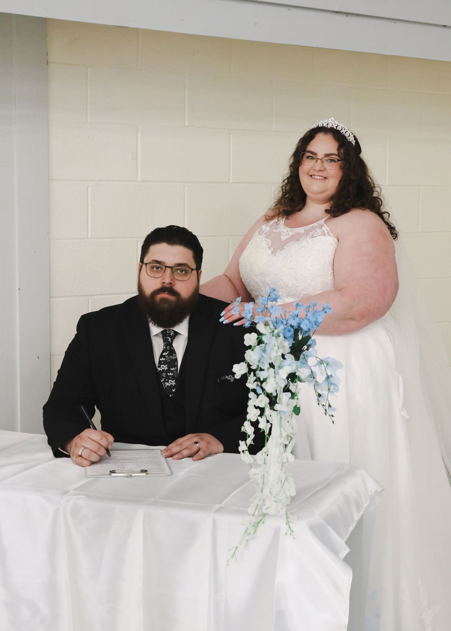 Bride and groom signing wedding documents at a white draped table.