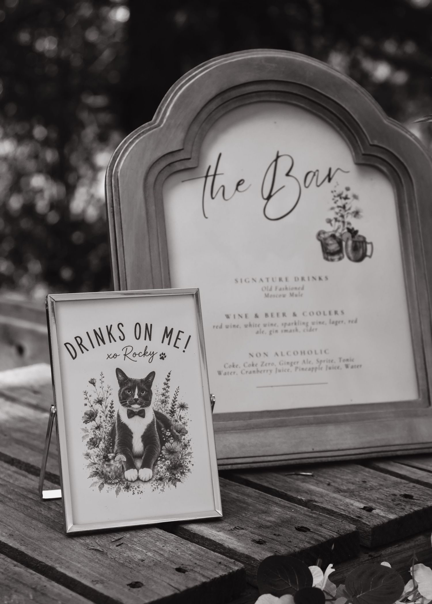 Black and white wedding bar sign with cat illustration reading Drinks On Me xo Rocky.