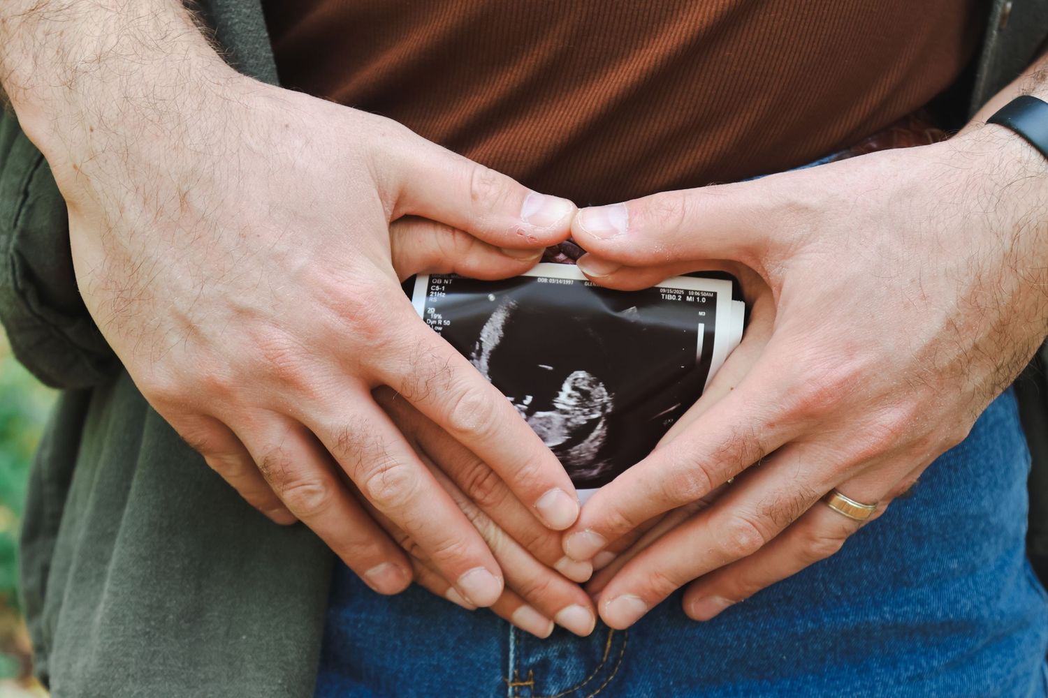 Close-up of couple forming heart shape with hands around ultrasound photo on pregnant belly.