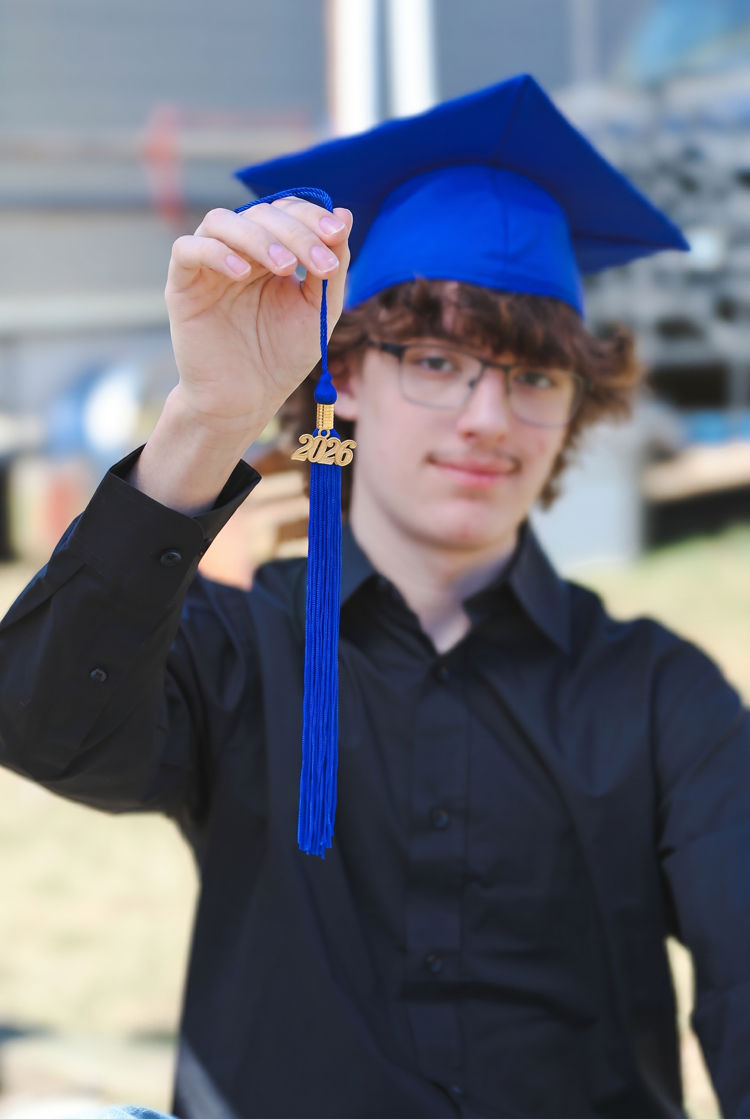 Graduating senior holding up blue 2026 tassel while wearing graduation cap for celebratory photo.
