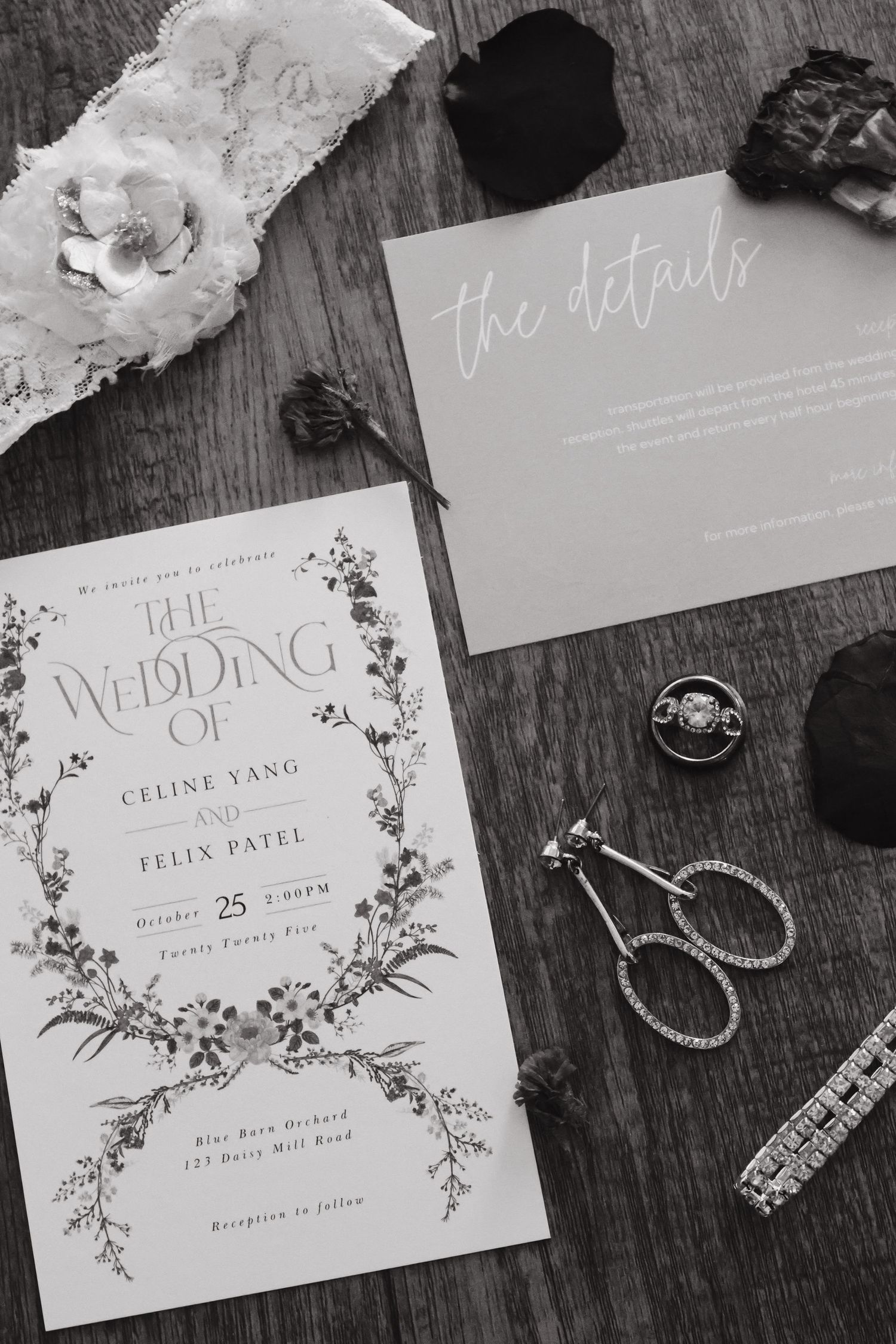 Black and white wedding invitation suitel with floral details, rings, and earrings on wood.