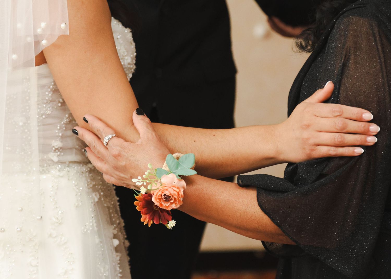 Bride receiving a floral wrist corsage with peach roses and teal ribbon on her wedding day.