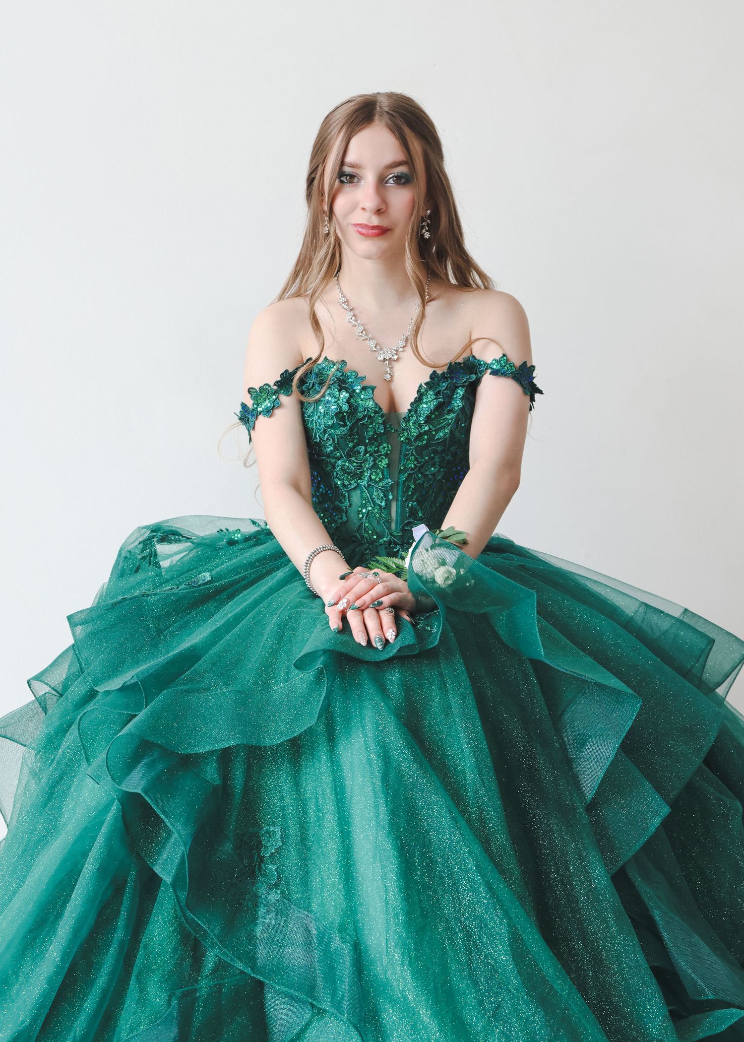 Young woman in emerald green off-shoulder ball gown with floral appliques and layered tulle skirt.