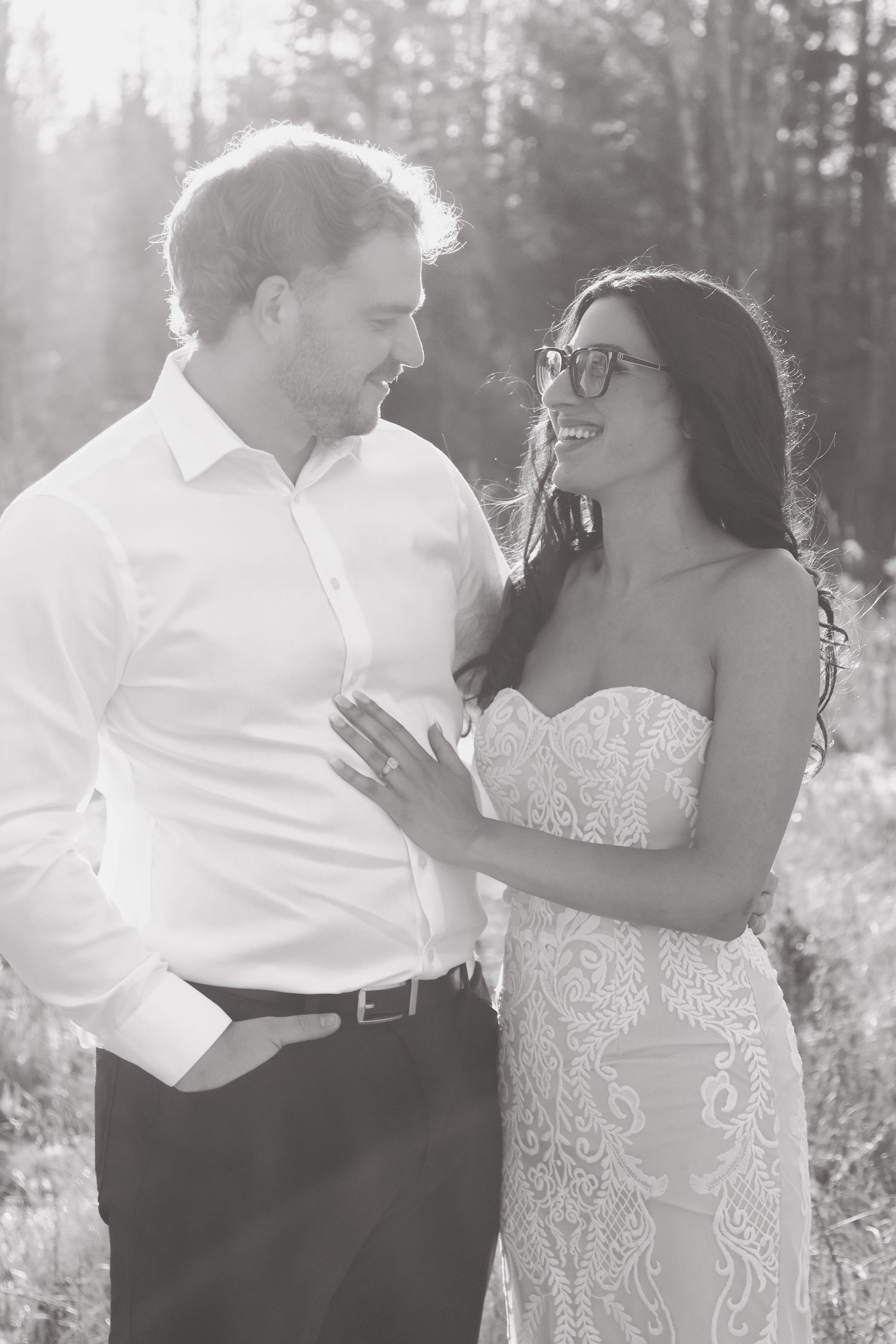 Black and white portrait of bride and groom sharing a romantic moment in sunlit forest.