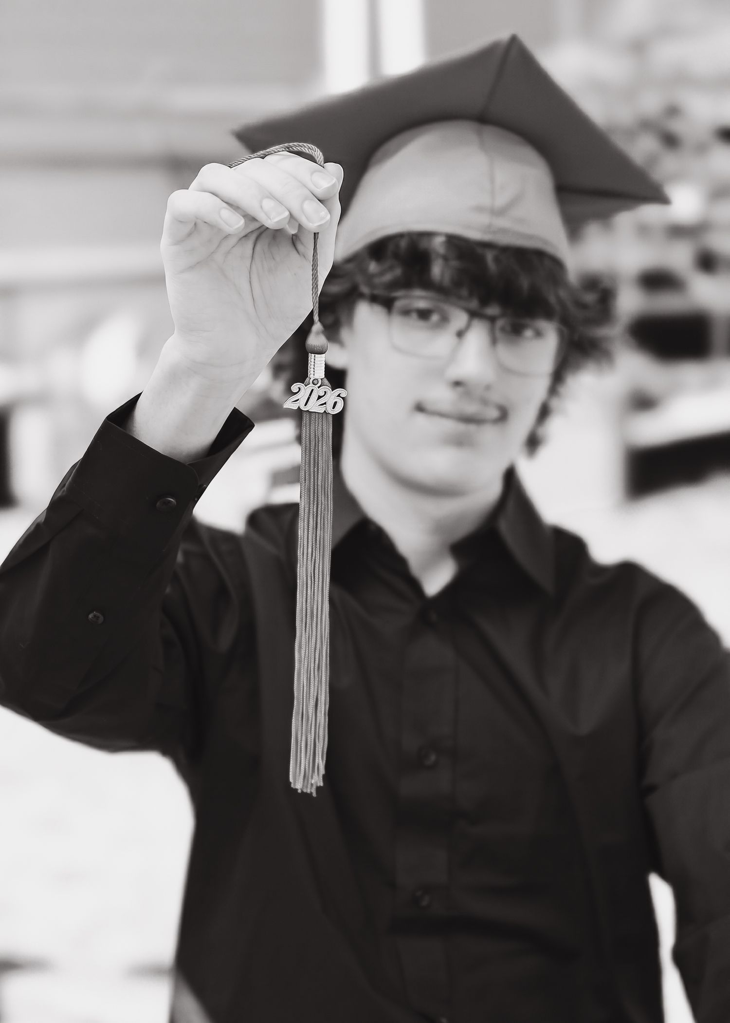 Black and white photo of young male graduate holding 2026 graduation tassel wearing cap.