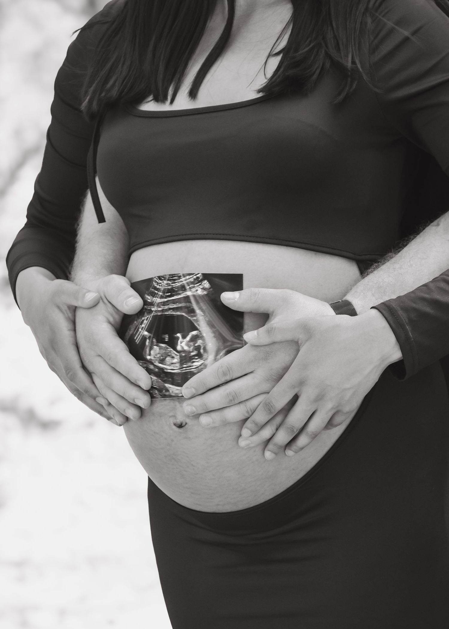 Black and white maternity photo of couple holding ultrasound over pregnant belly.
