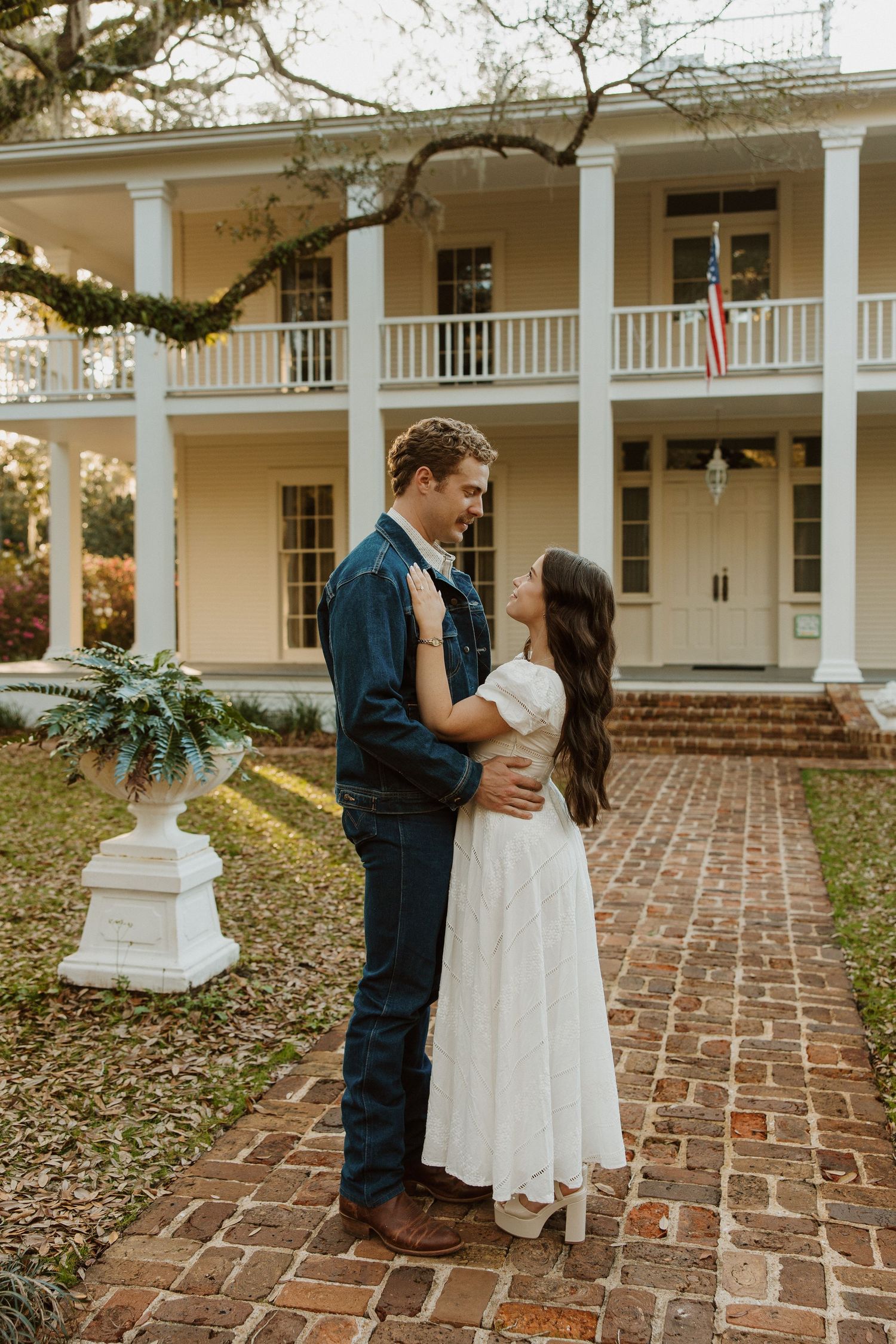 A romantic wedding couple shares intimate moments on a brick patio in front of a stately white columned southern mansion.