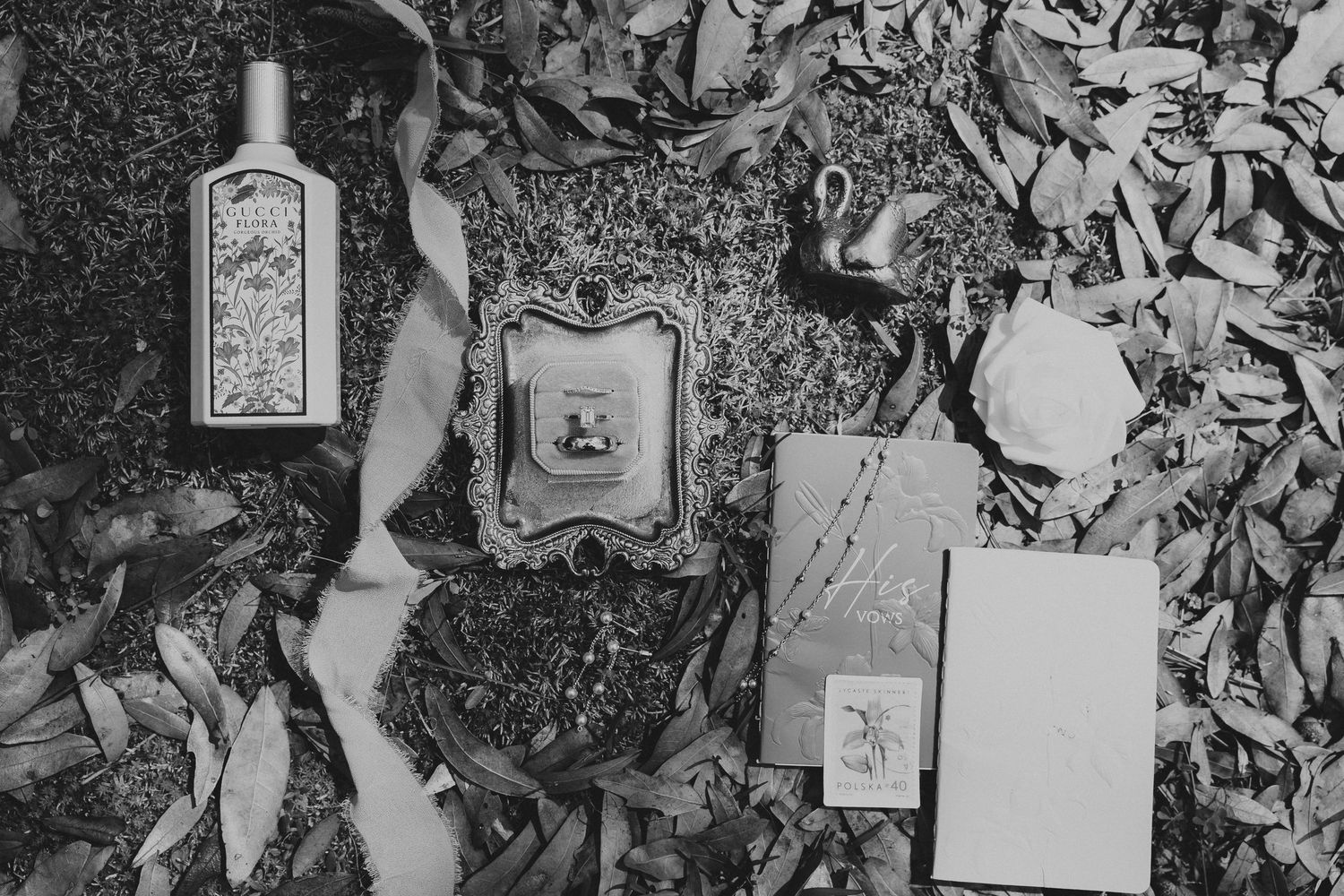 Black and white flat lay of vintage perfume bottle, ornate mirror, and antique cards on autumn leaves.