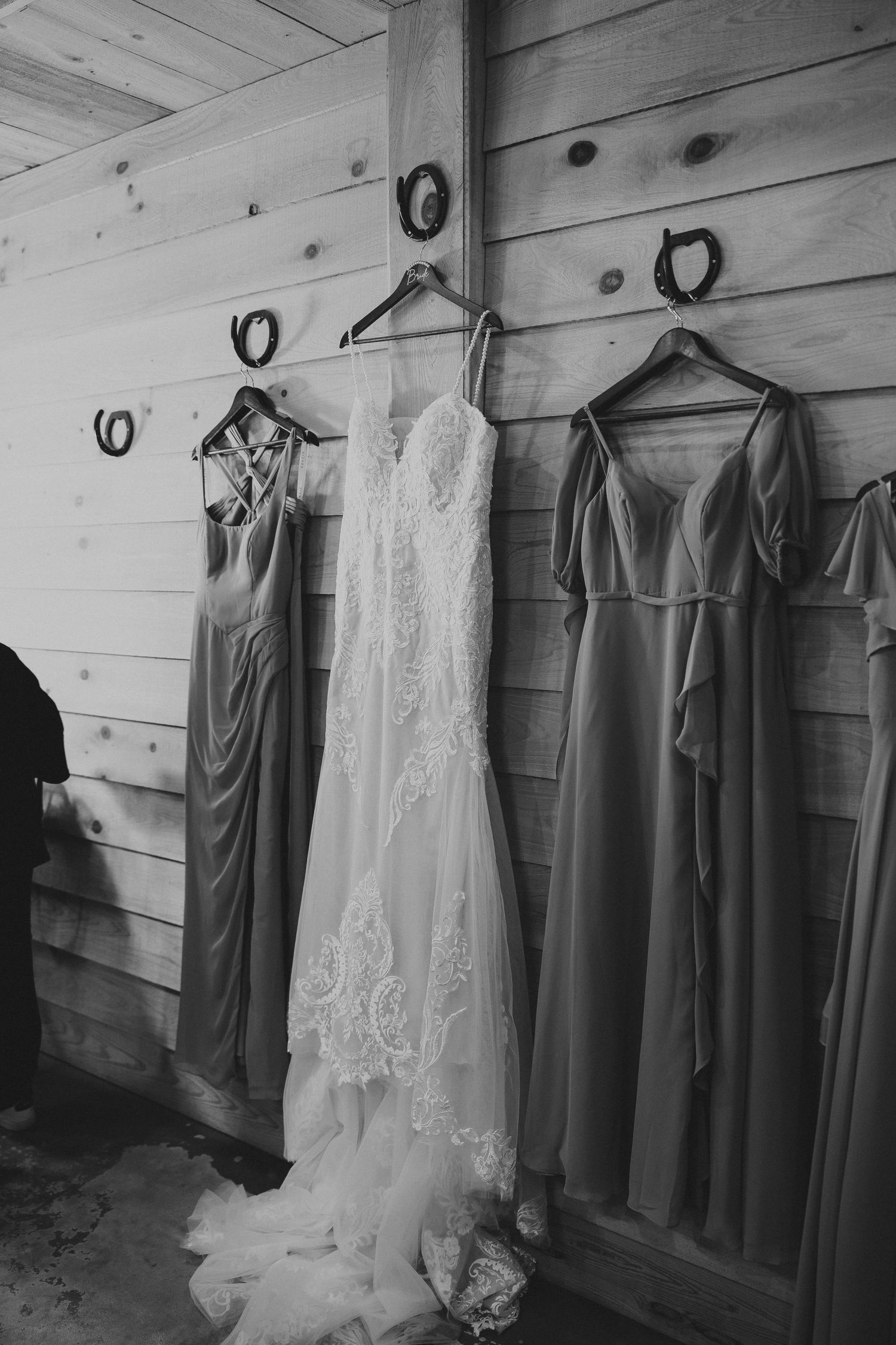 Wedding dress and bridesmaid dresses hanging on wooden wall in black and white.