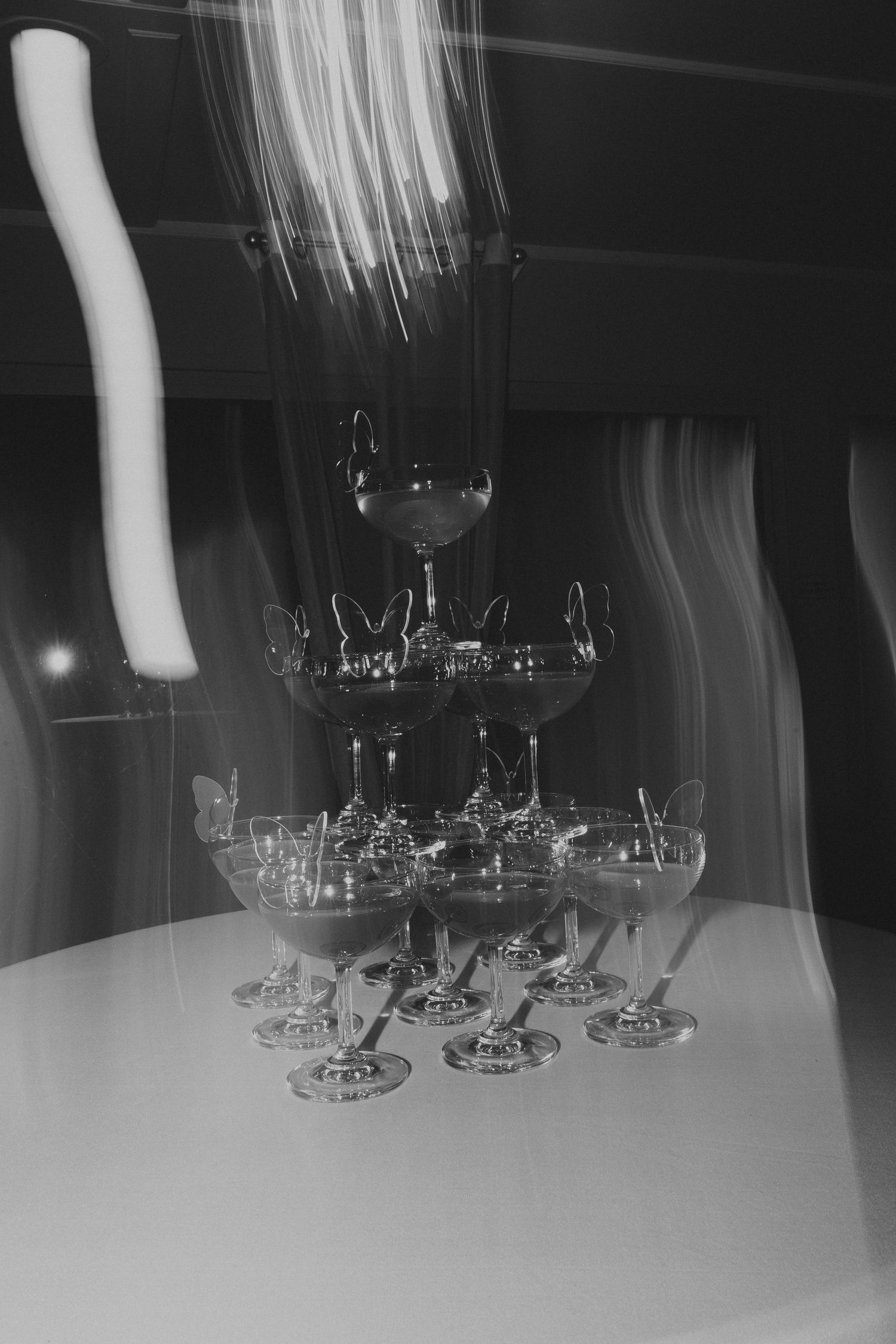 Black and white photo of wine glasses arranged on a table with motion blur effect.