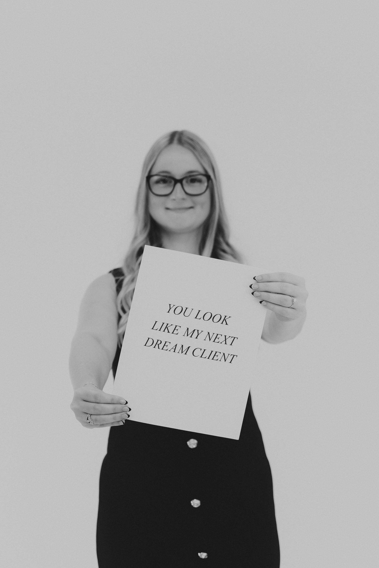 Photographer holding sign that says 'You look like my next dream client' in black and white.