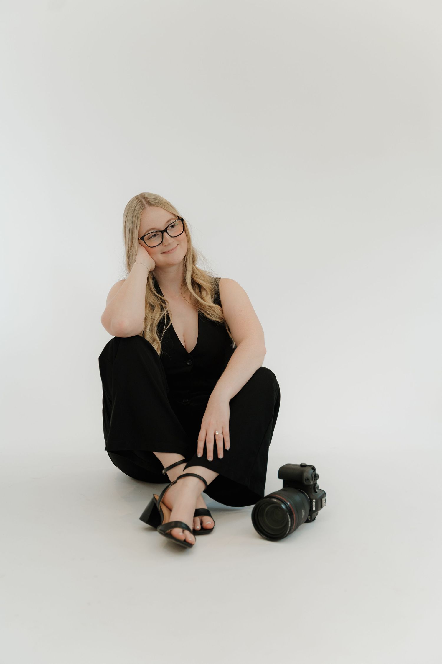 Person in black attire poses against white background in artistic portrait series showing different sitting positions.
