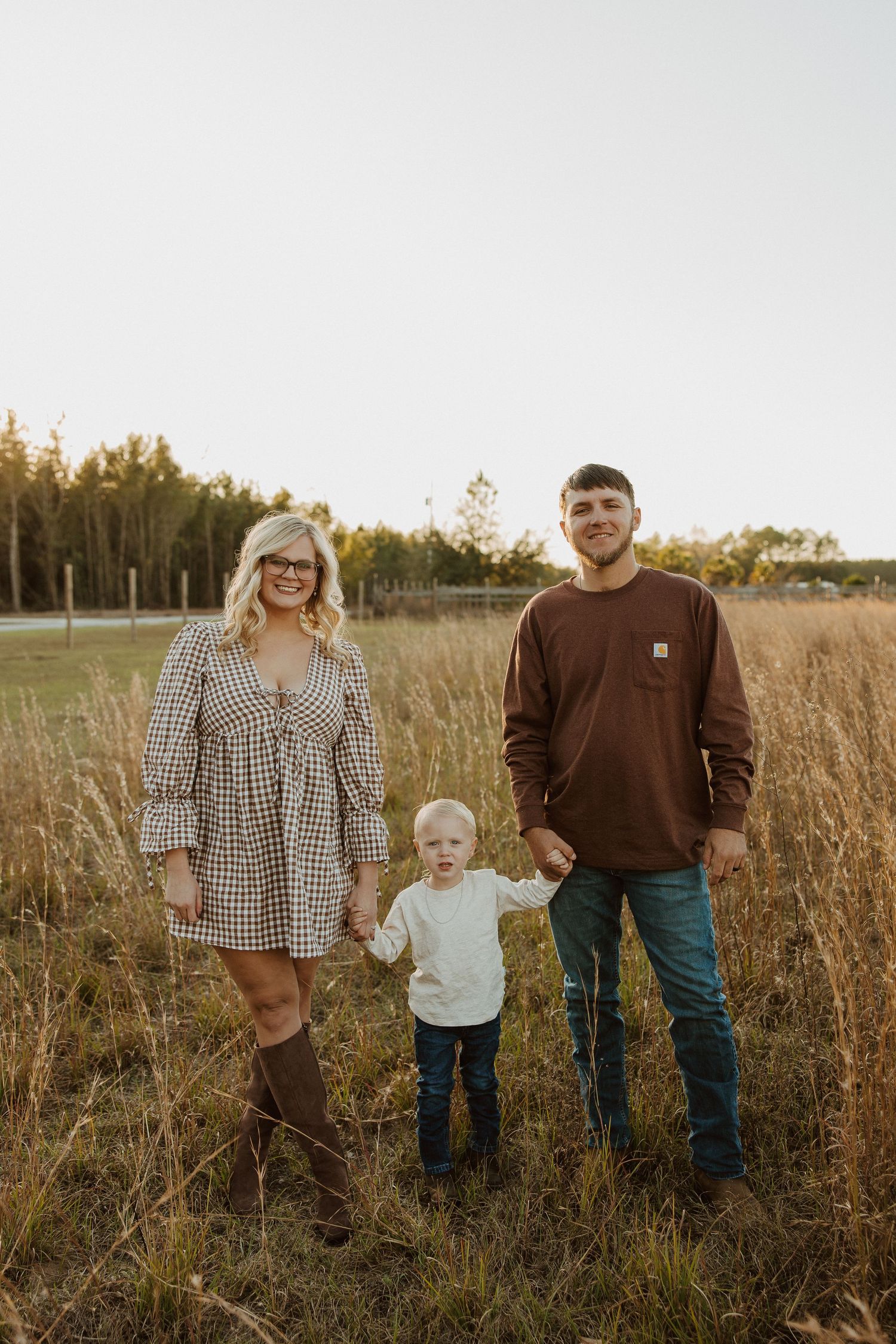 A family poses together in a rustic field with tall grass during sunset.