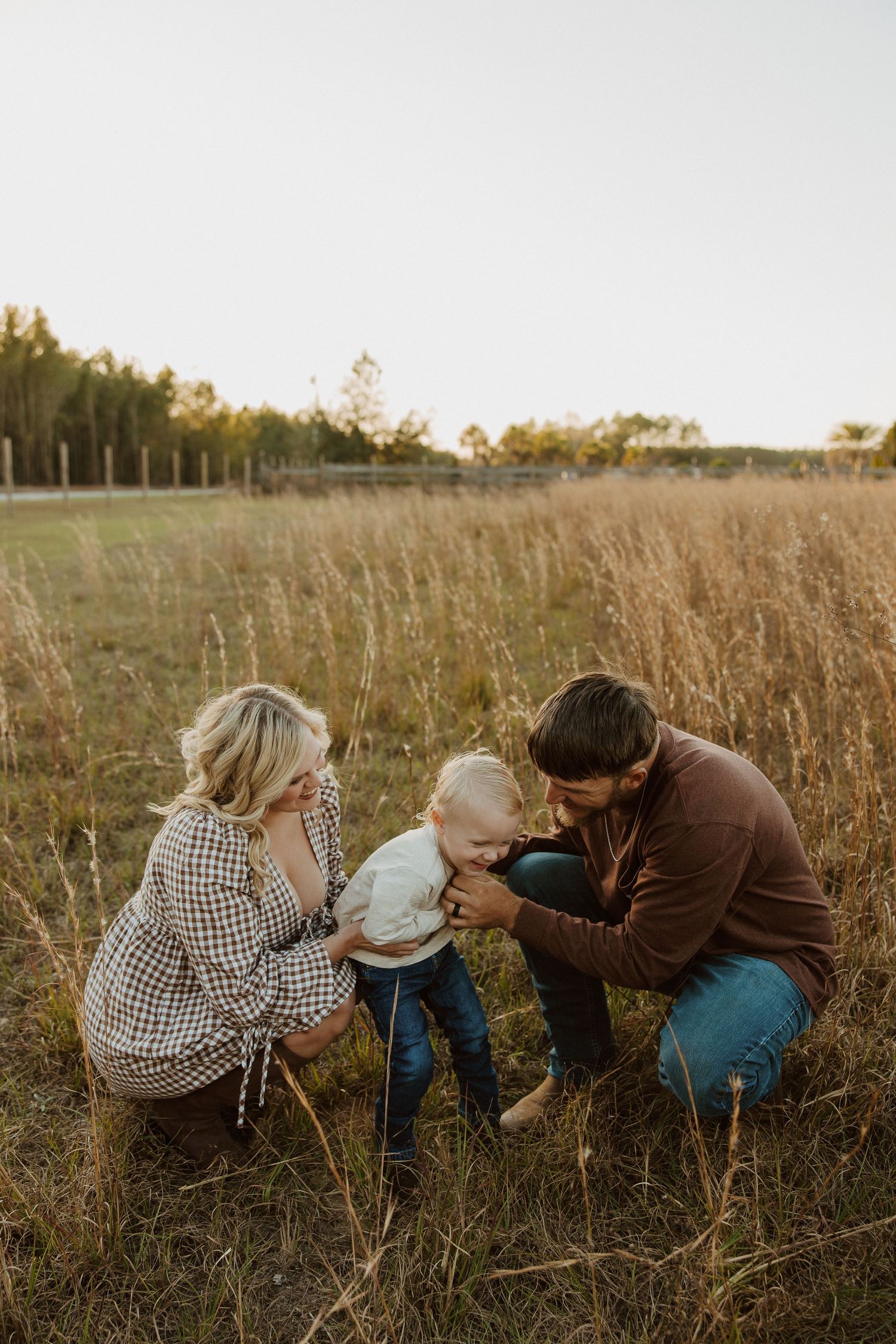 A family plays together while crouching in tall grass during sunset.