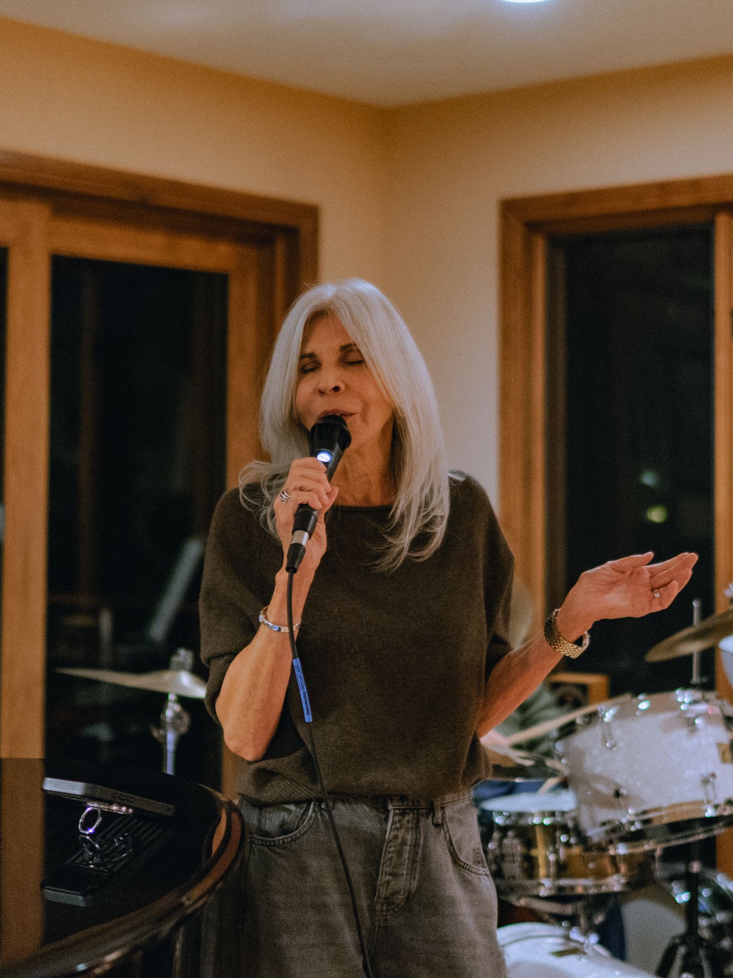Singer performing passionately in front of a drum kit in warm indoor lighting.