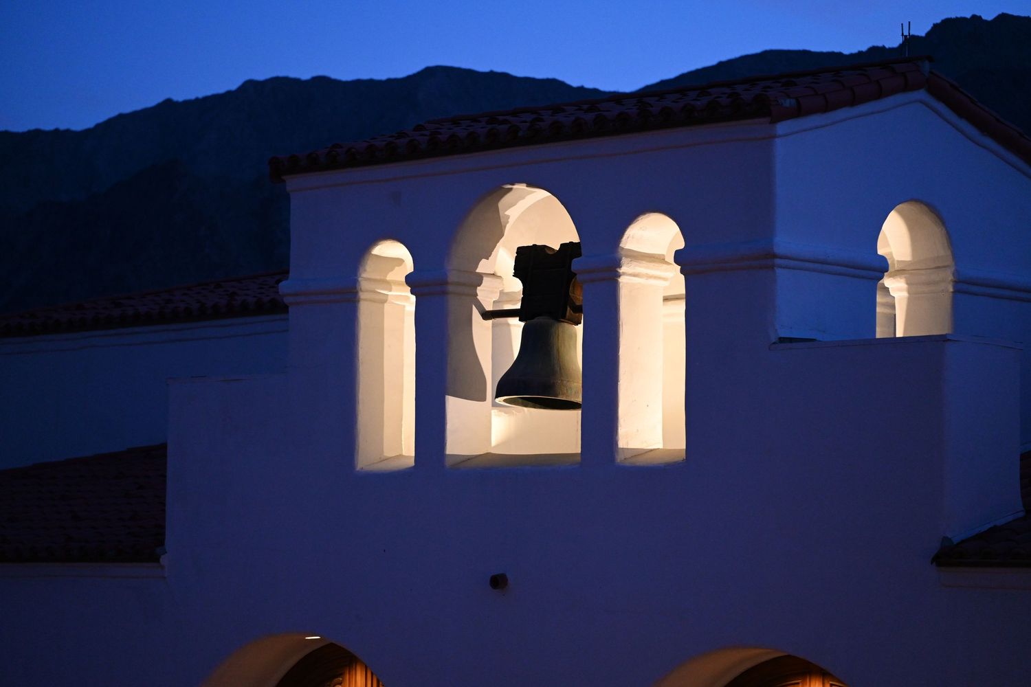 An illuminated bell tower with white arches against a dusky blue mountain backdrop.