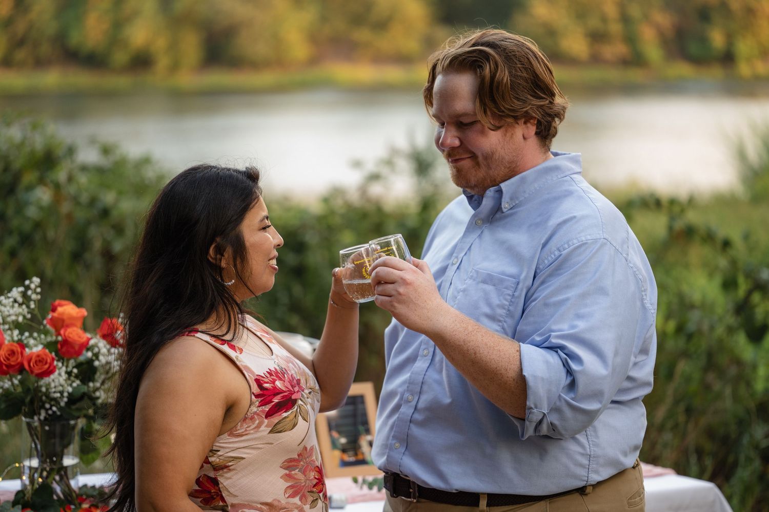 Couple sharing intimate moments during golden hour by a lake with decorative setup.