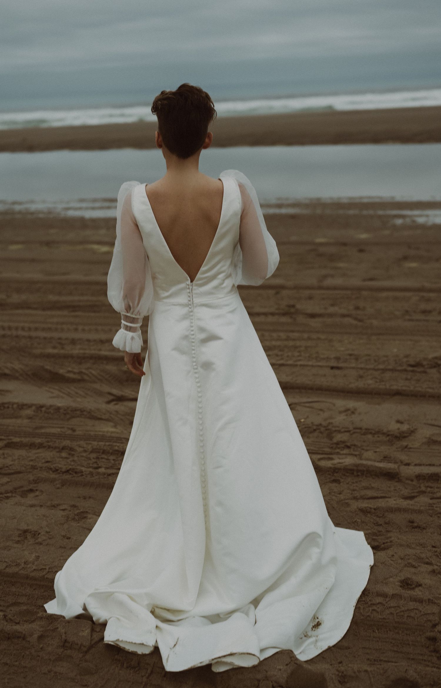 A flowing white wedding dress with ruffled details photographed on a beach.