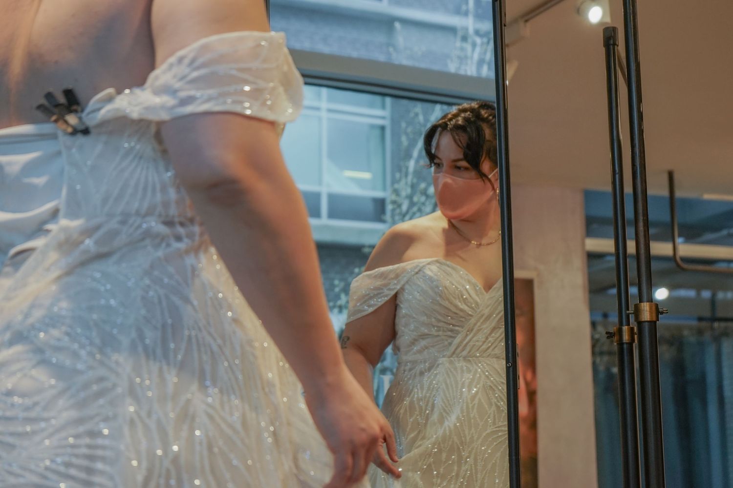 A white wedding dress being fitted and adjusted in a bridal boutique with natural lighting.