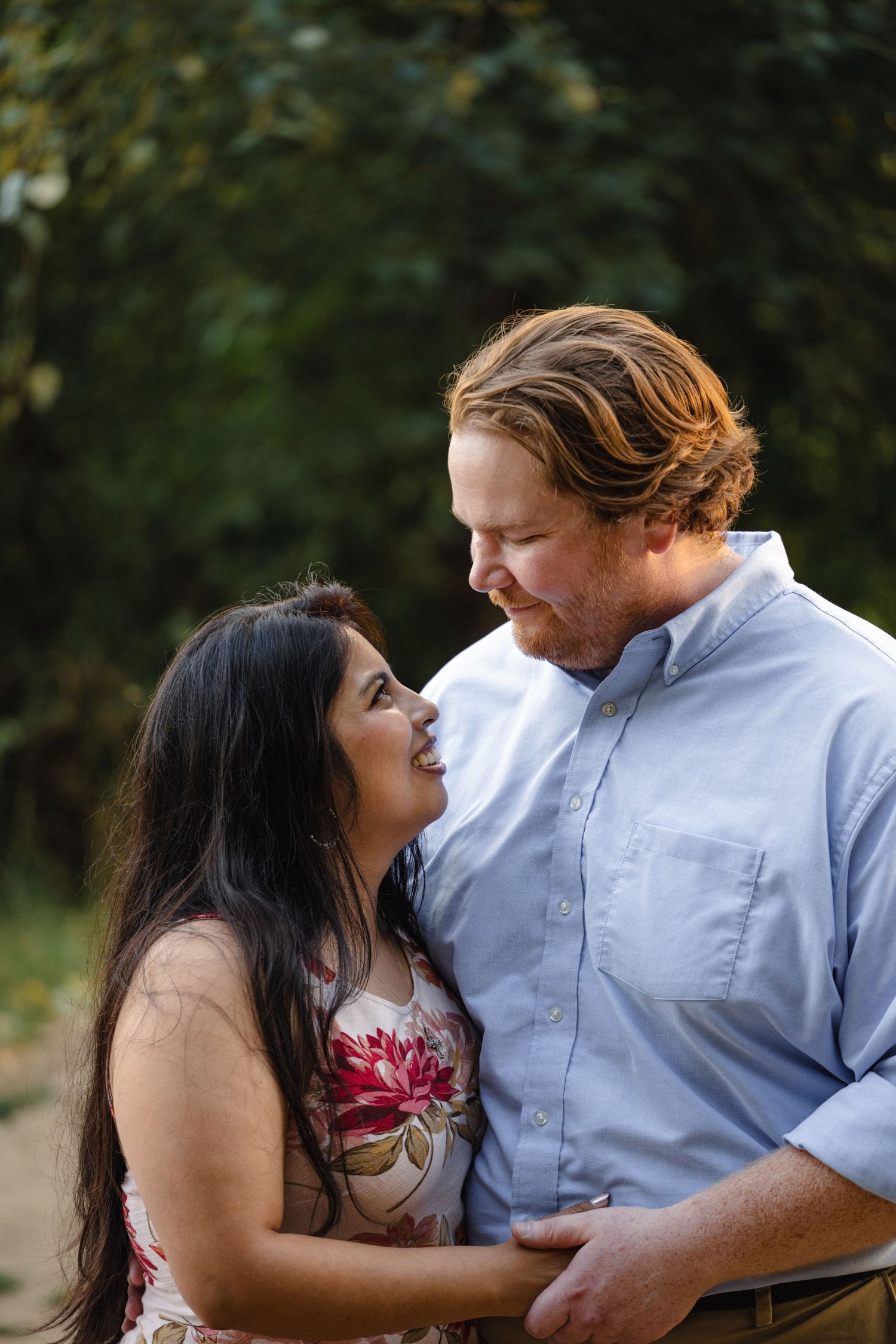 A romantic couple shares tender moments in an outdoor photo series with natural lighting and greenery in the background.