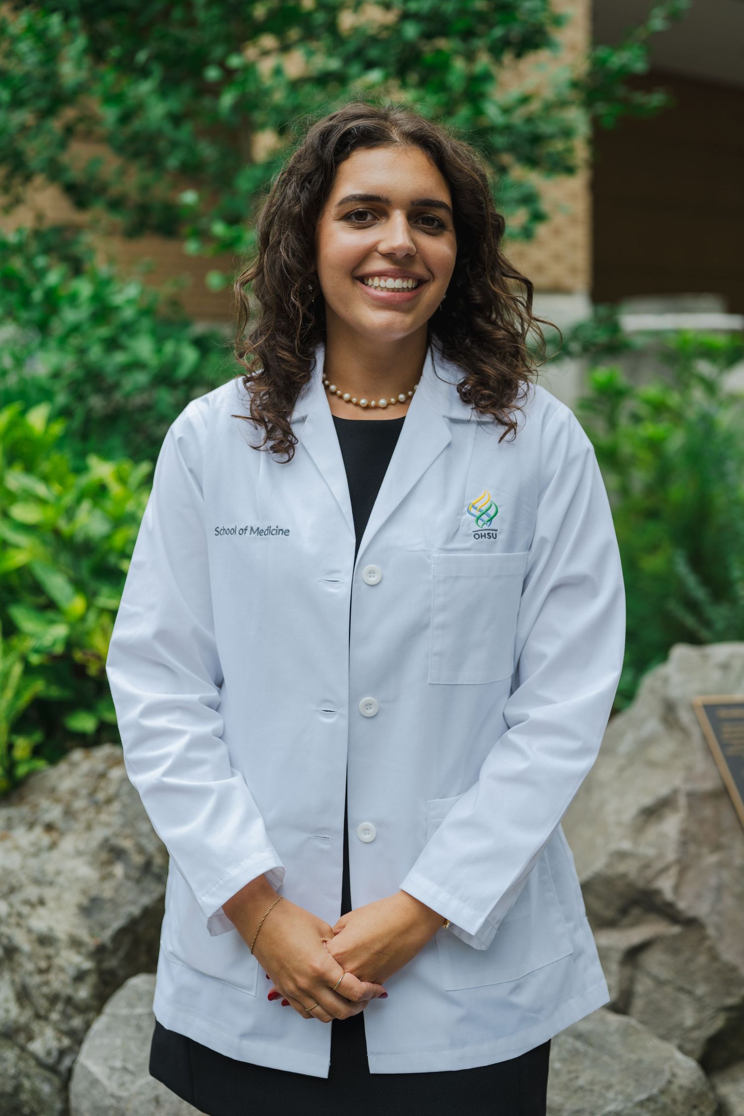 Healthcare professional in white coat posing outdoors near decorative rock landscaping.