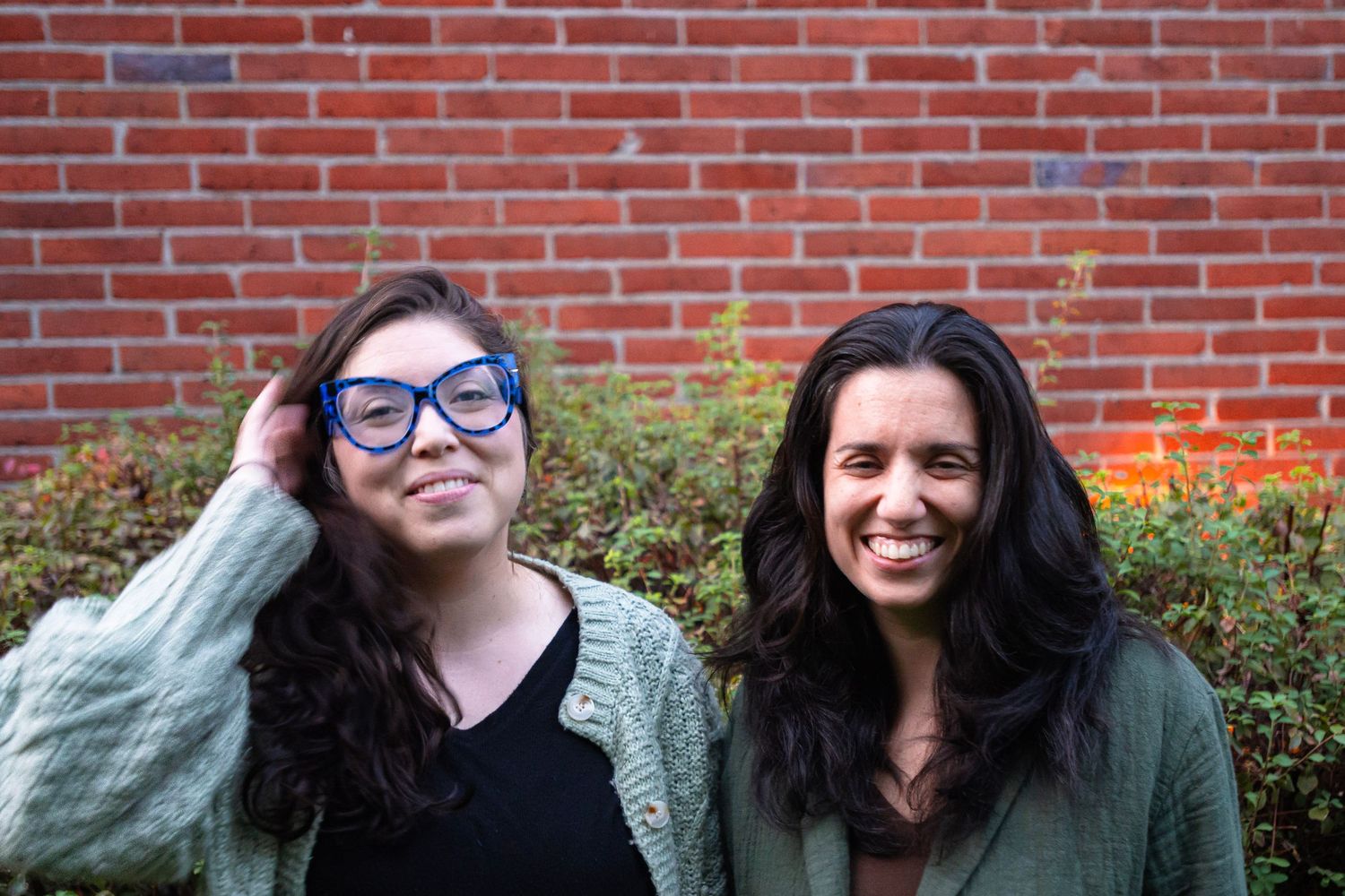 Two people posing in front of a red brick wall.