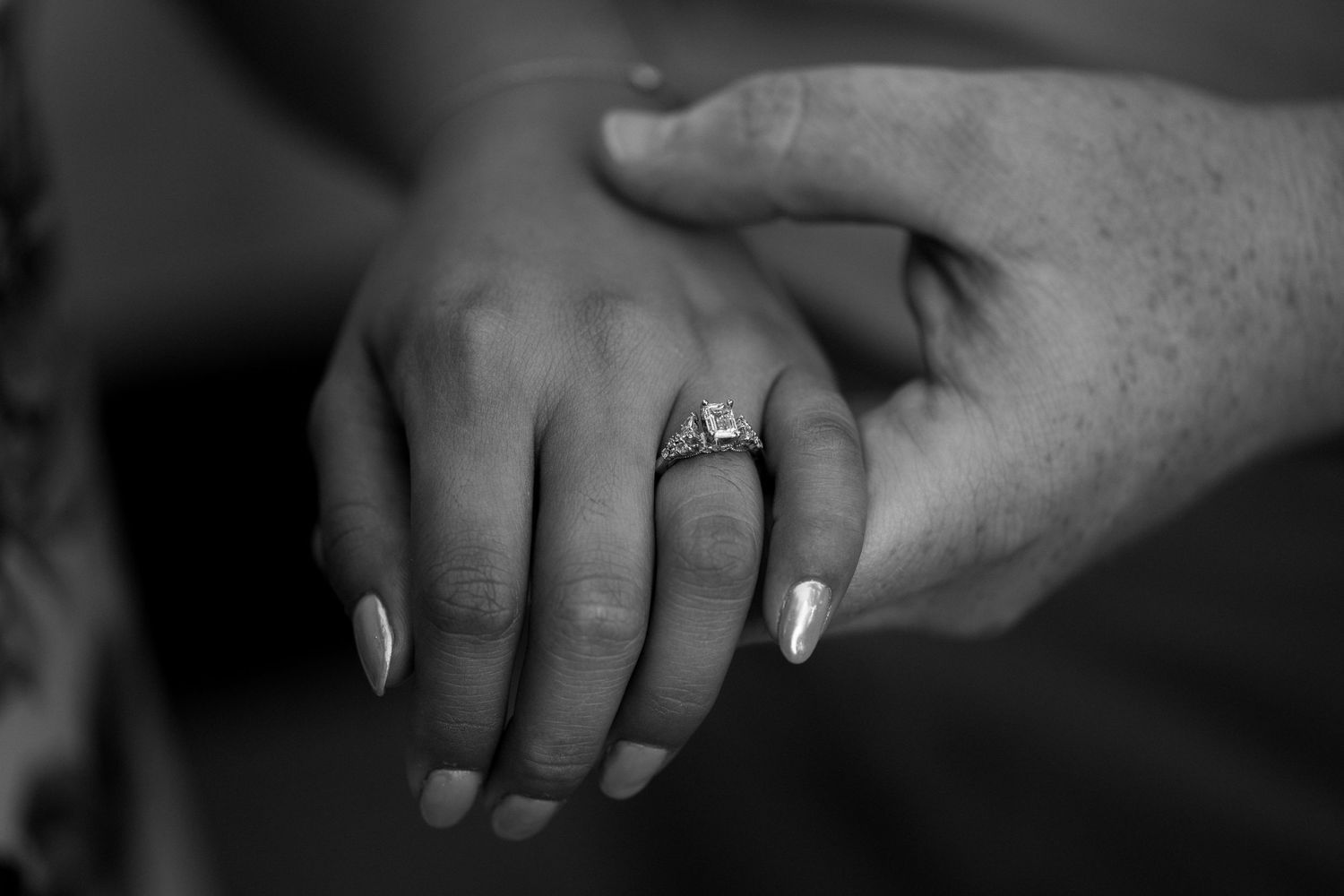 Close-up black and white photo of hands with engagement ring.