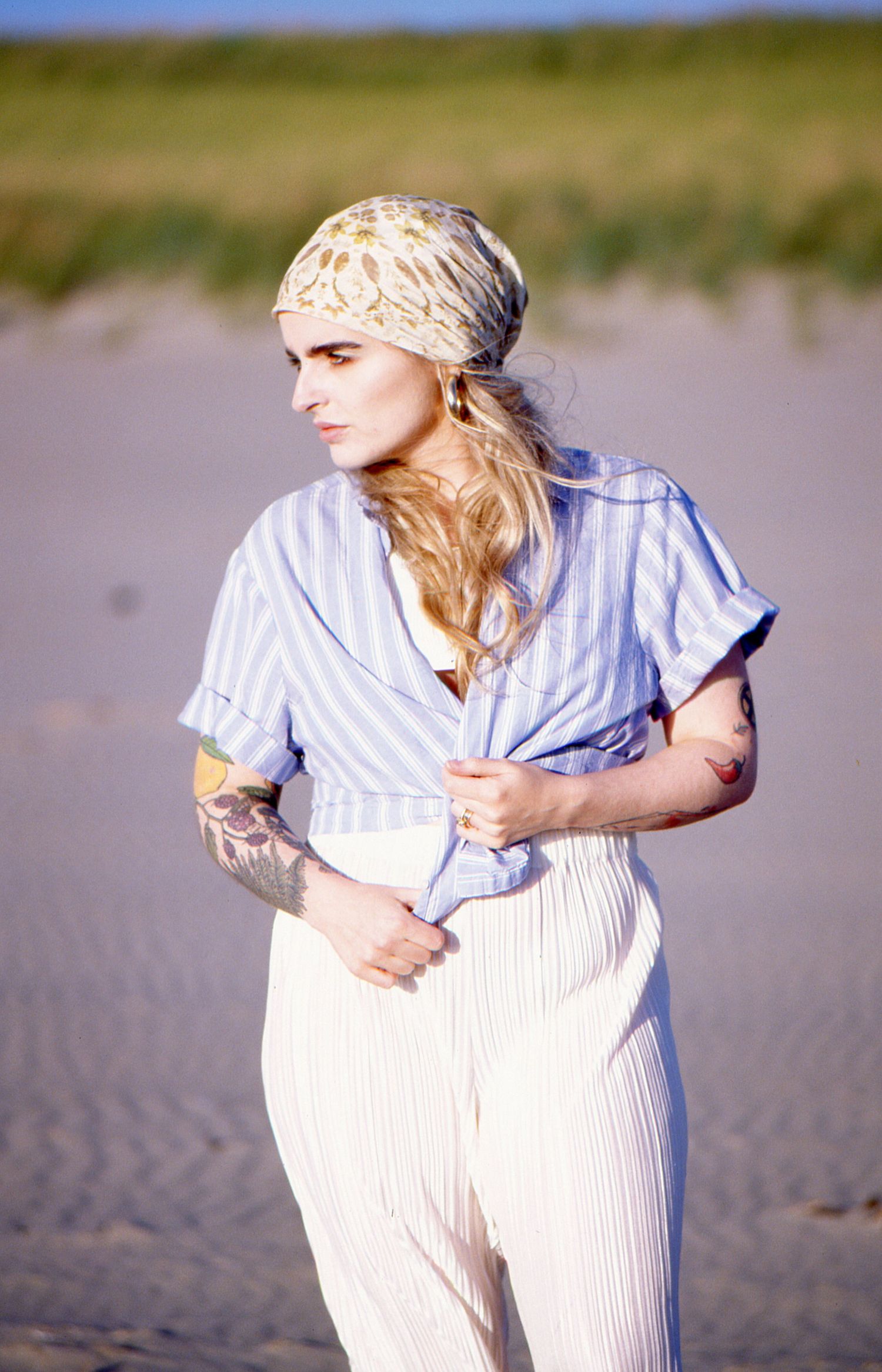 A person in striped white clothing poses on a beach during golden hour.
