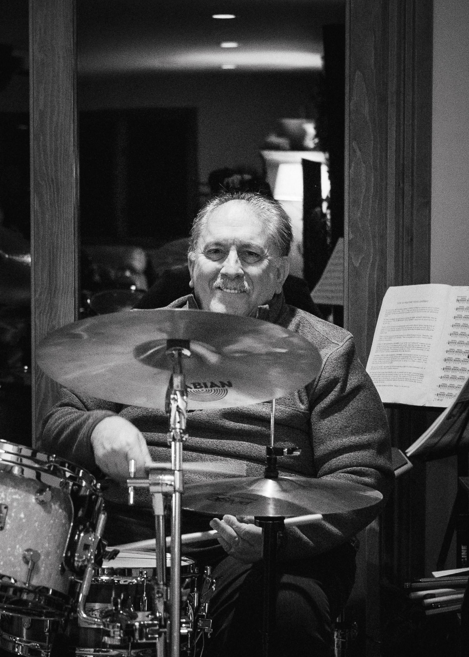 Drummer performing behind a professional drum kit with cymbals and sheet music visible.