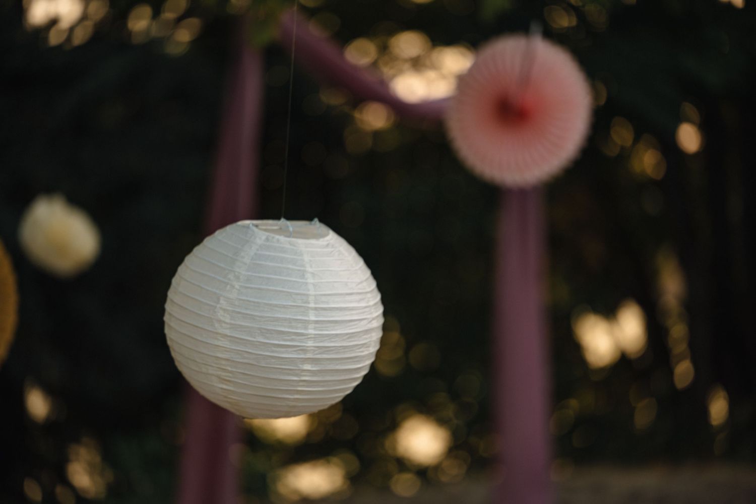 White paper lanterns hang from trees at sunset creating a romantic outdoor setting.