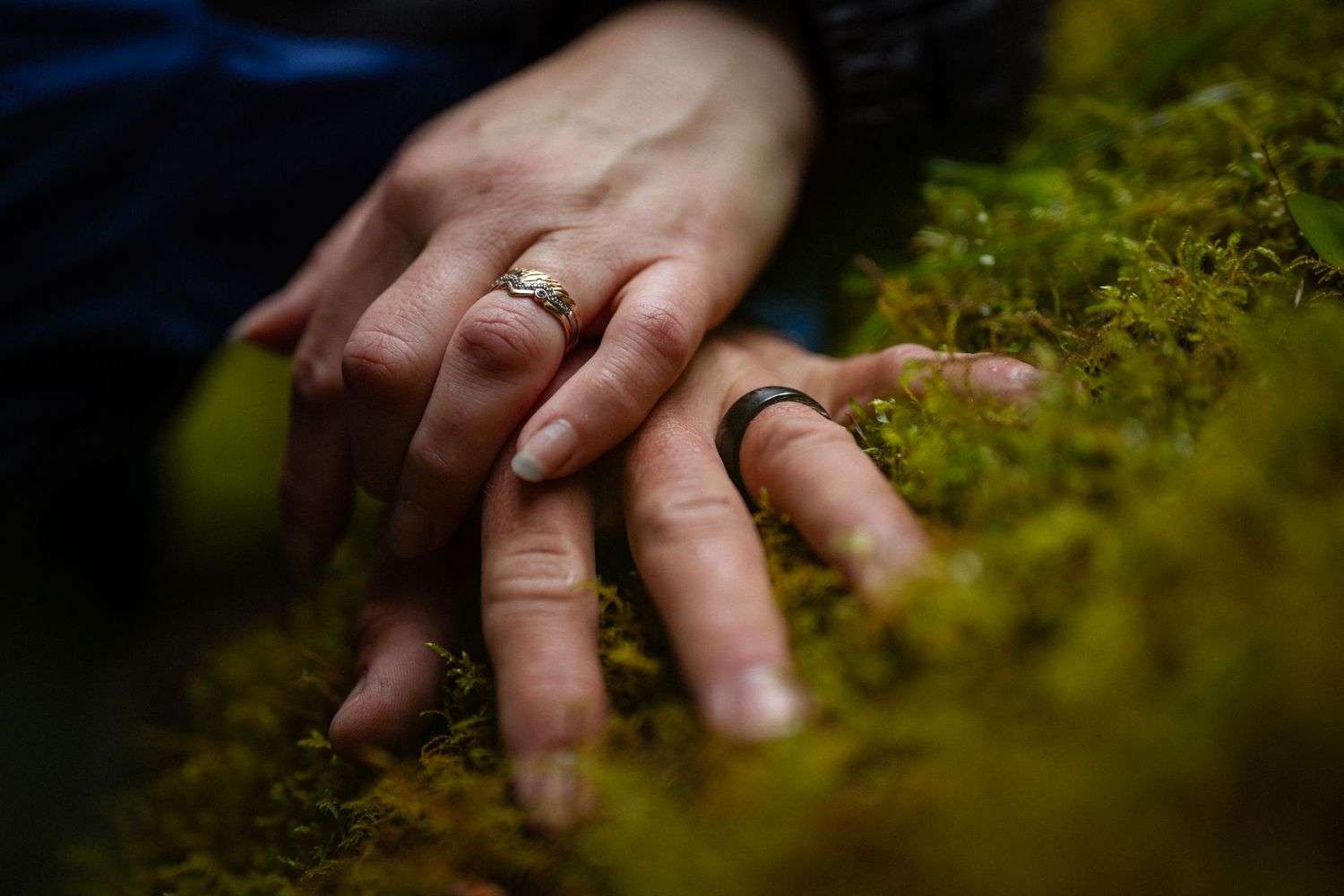 Two hands with wedding rings resting on green moss, symbolizing love and commitment in nature.
