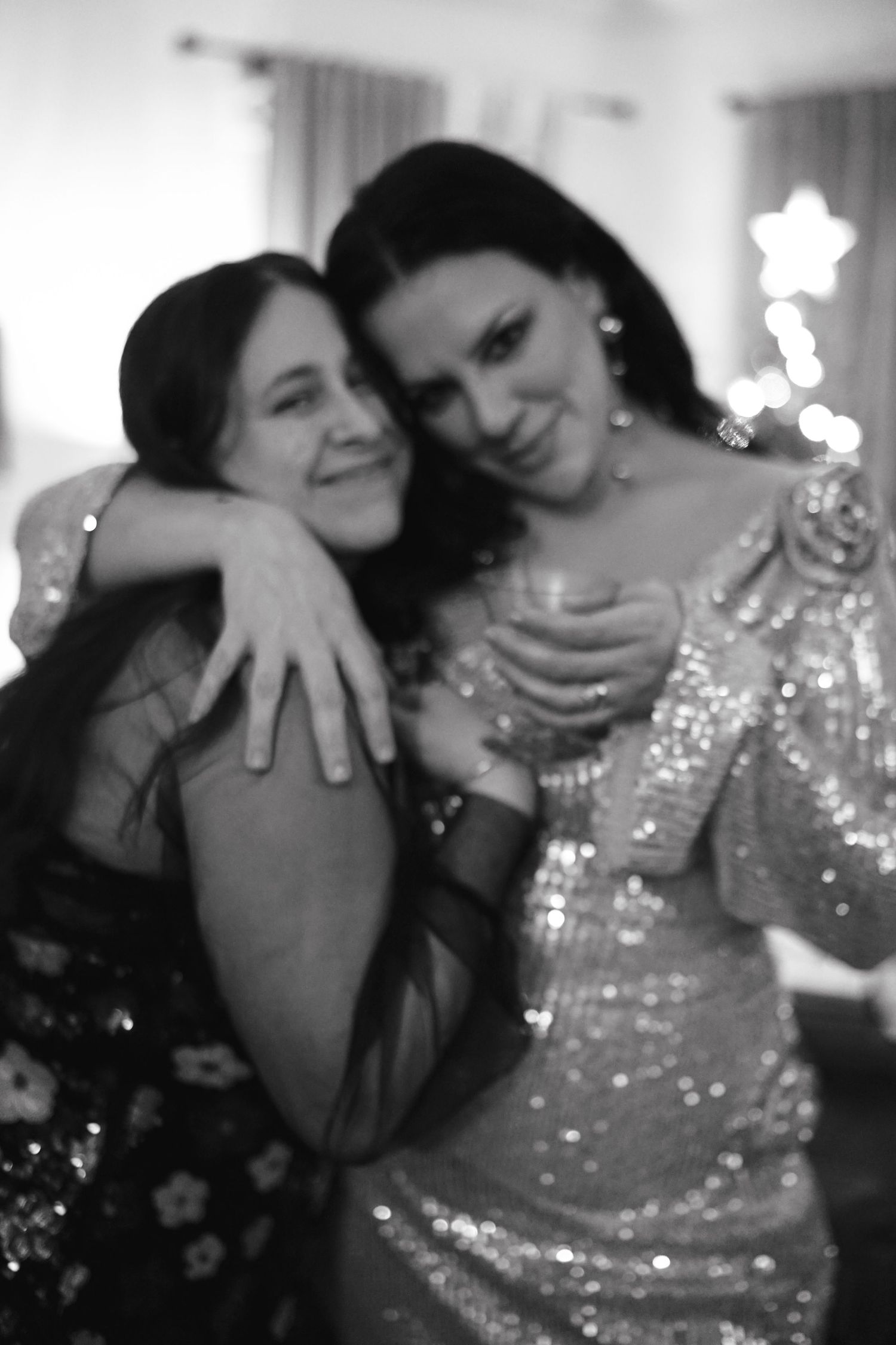 Two guests in sparkly evening attire share a warm embrace at a celebration.