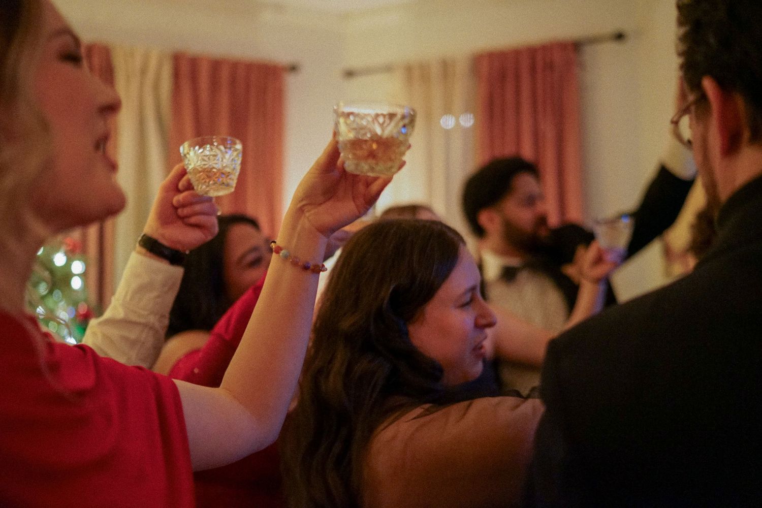 Celebratory scene with raised glasses during a festive toast at an indoor gathering.