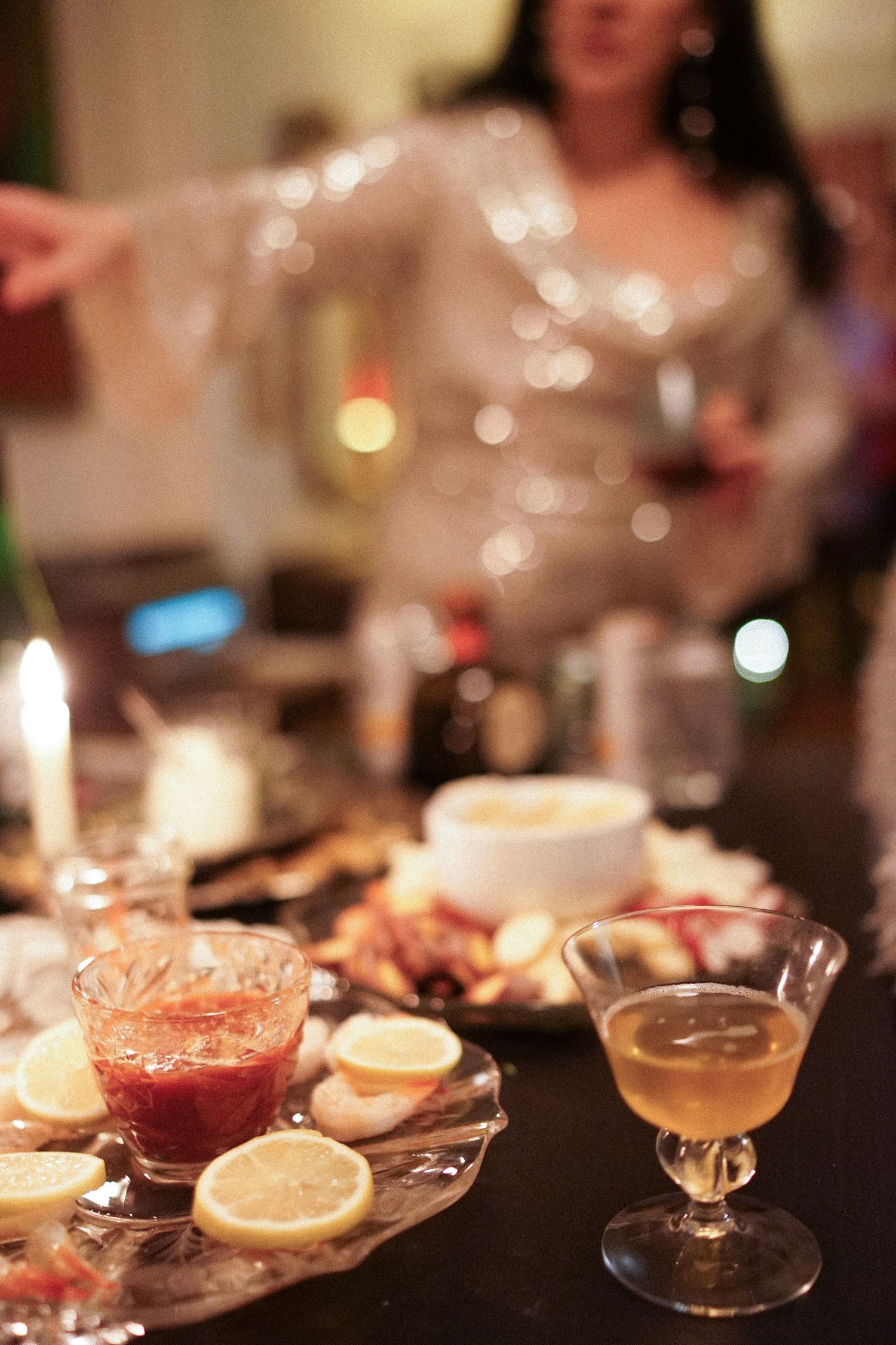 Elegant cocktails and appetizers served on a table with candlelight and bokeh effects.