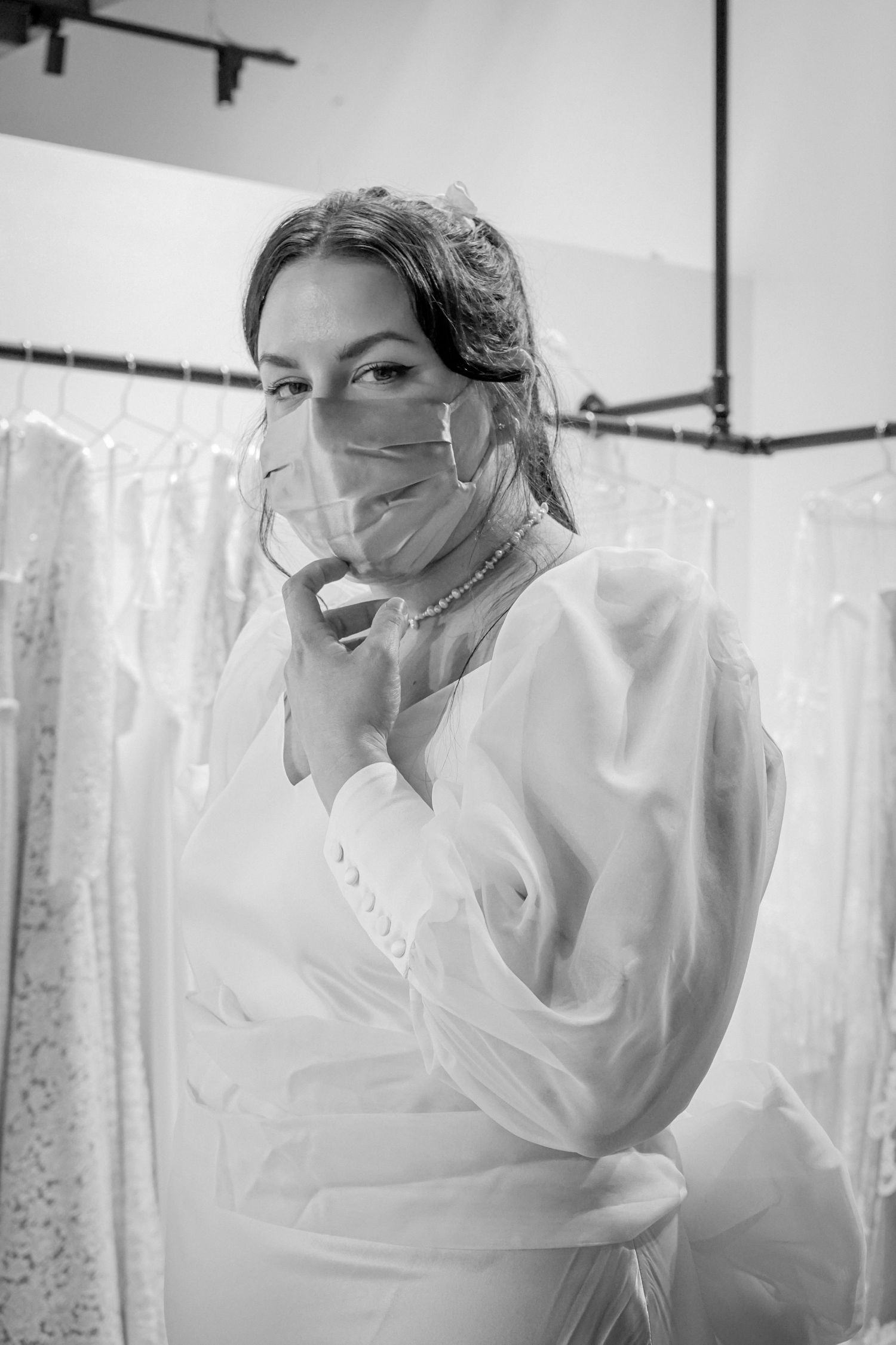 Healthcare worker in protective gear and mask by window curtains in black and white.