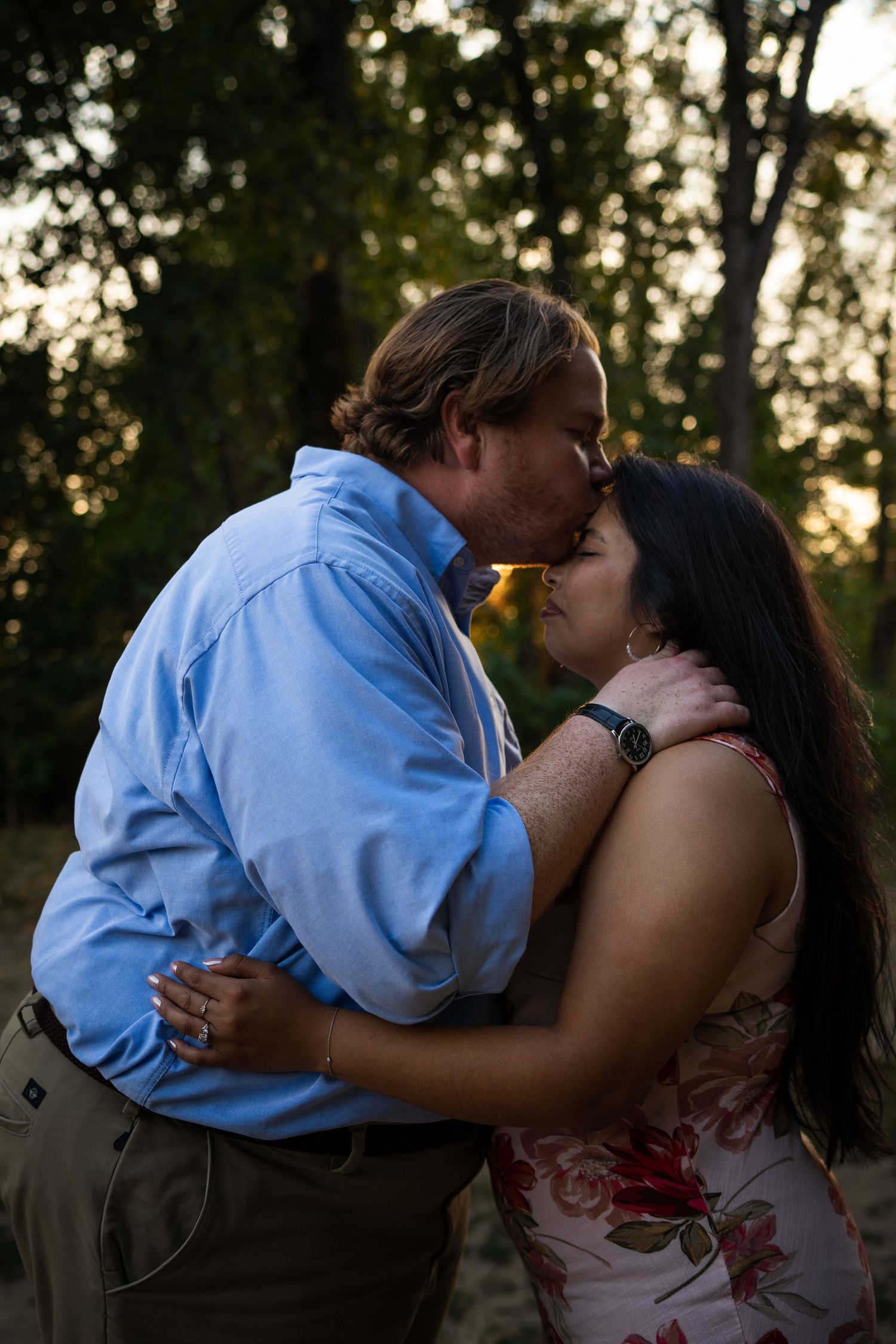 A romantic couple embraces during a sunset photoshoot in a natural outdoor setting.