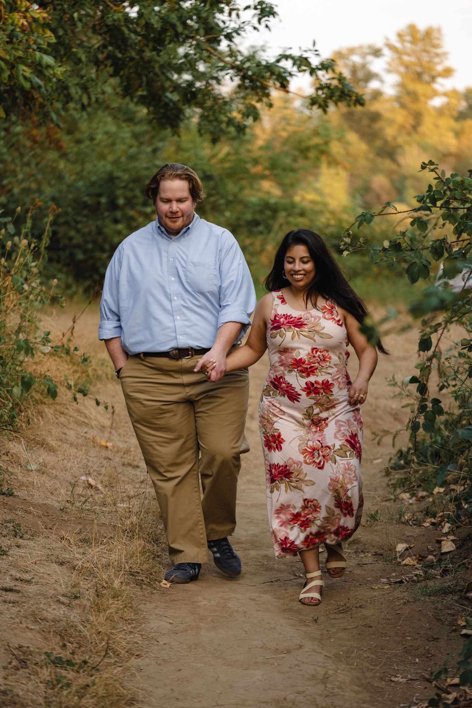 Couple walking together on a dirt path through autumn foliage.