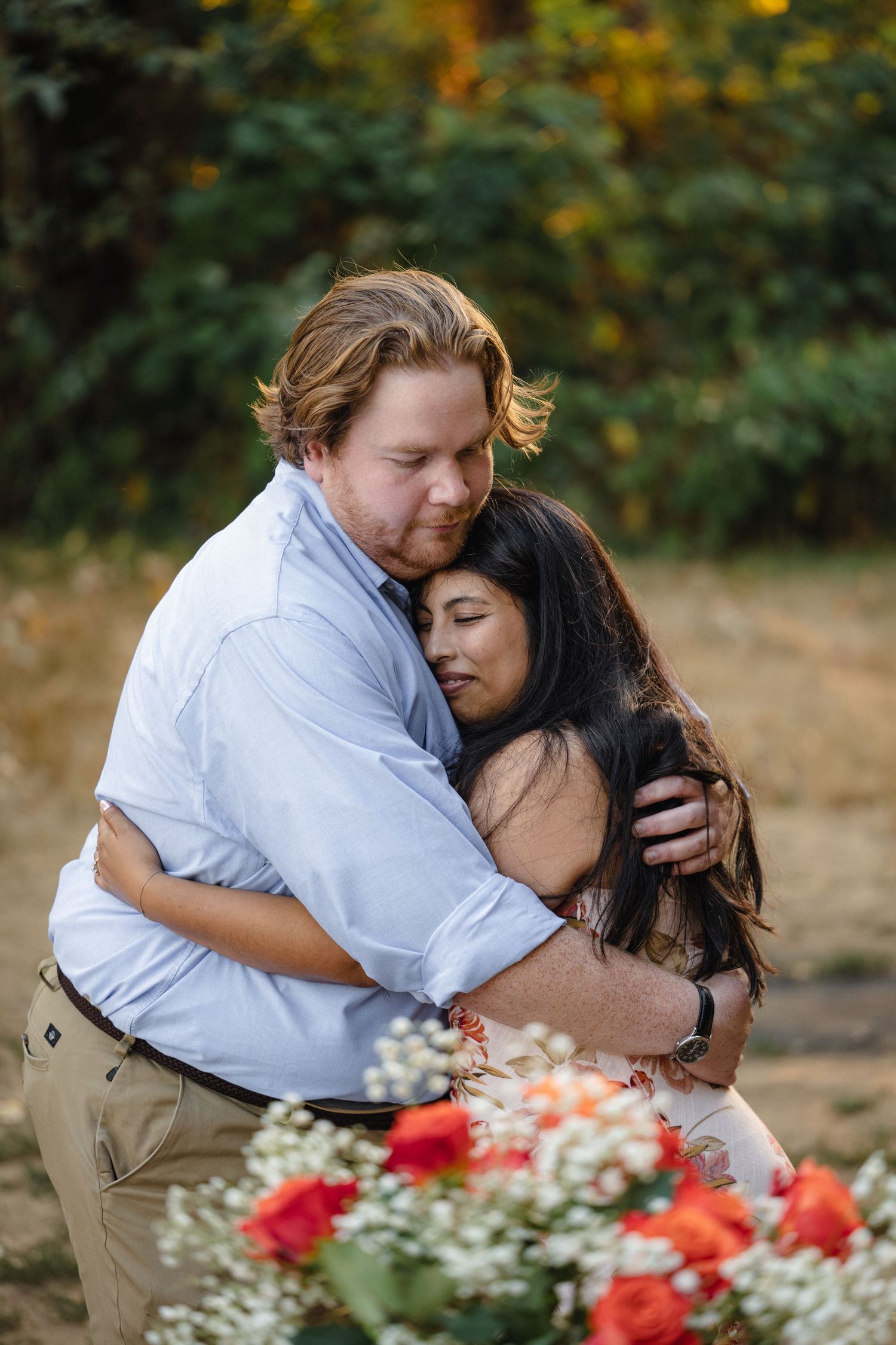 Couple embracing near red flowers during an outdoor photoshoot.