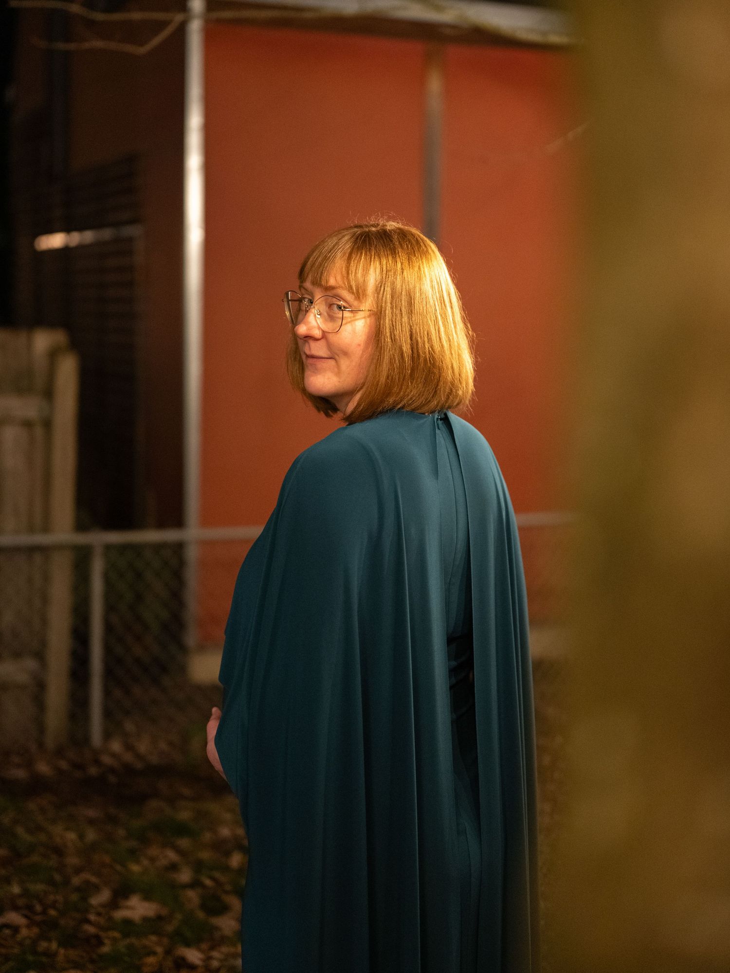 Person wearing a teal dress stands in warm autumn lighting outdoors.