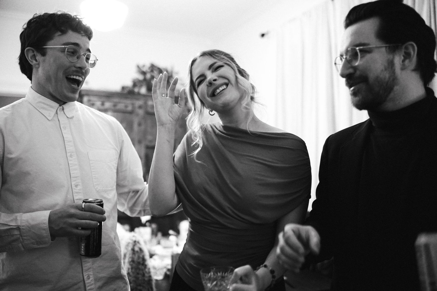 Three friends laugh together at a casual indoor gathering.