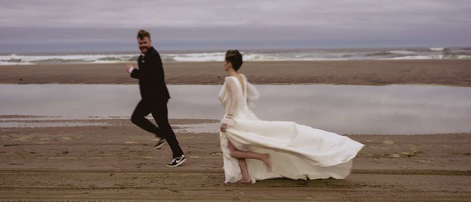 Couple running along a misty beach with flowing wedding dress.