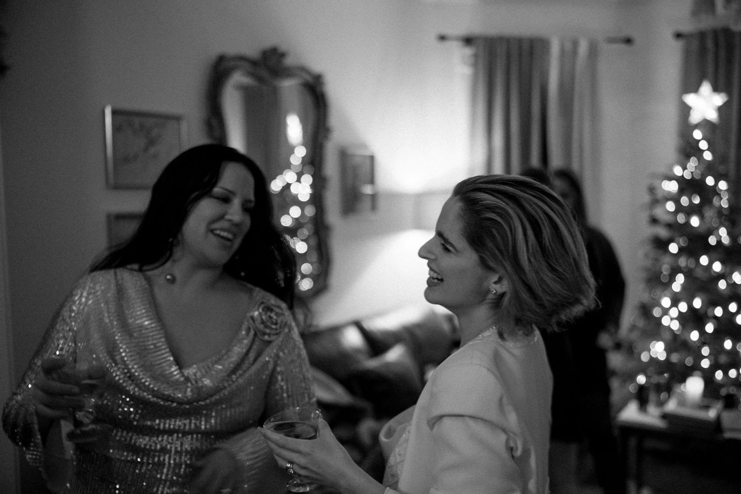 Two people share a joyful conversation at a Christmas party with decorated trees in background.