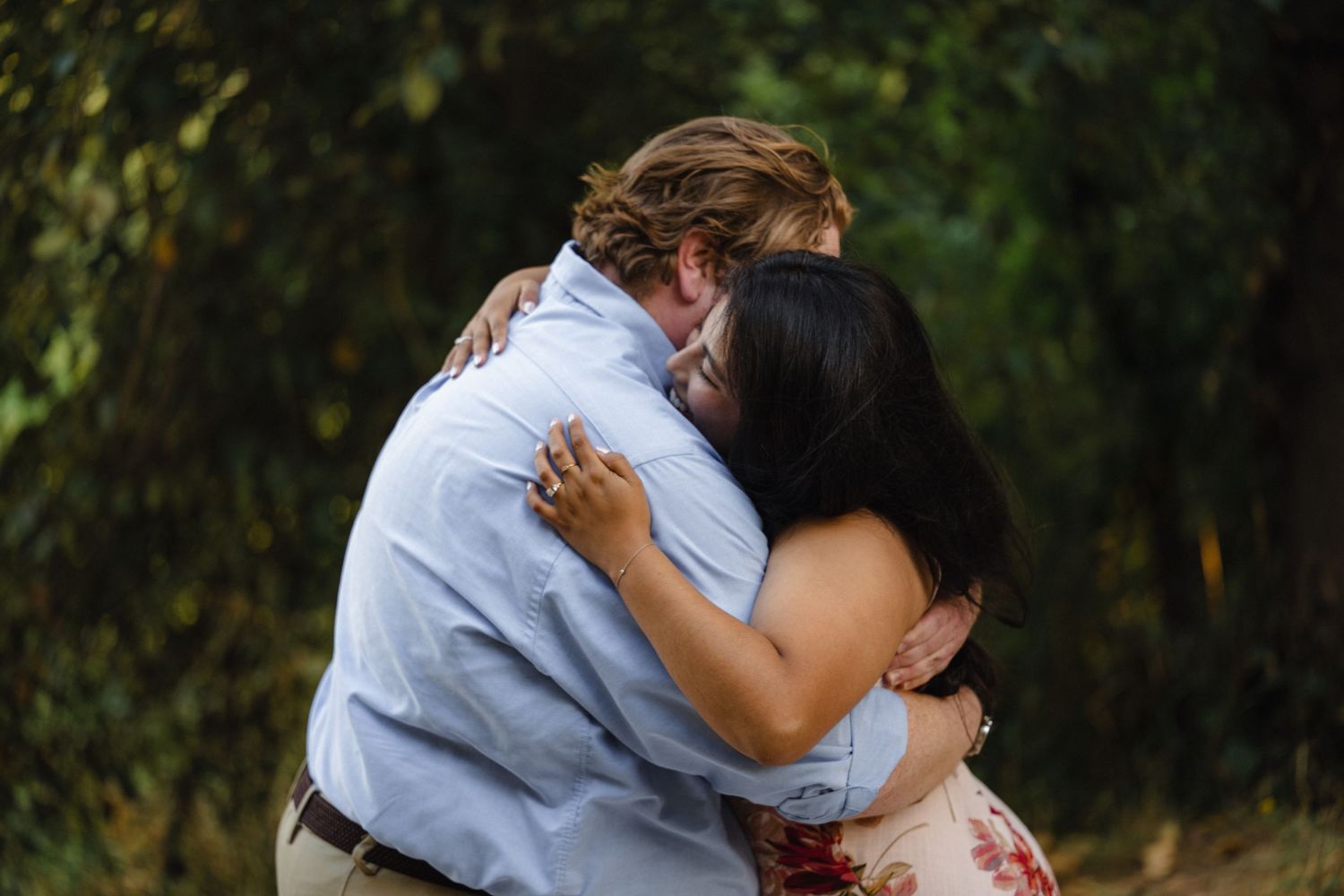 Couple embracing in a romantic outdoor setting with natural greenery.