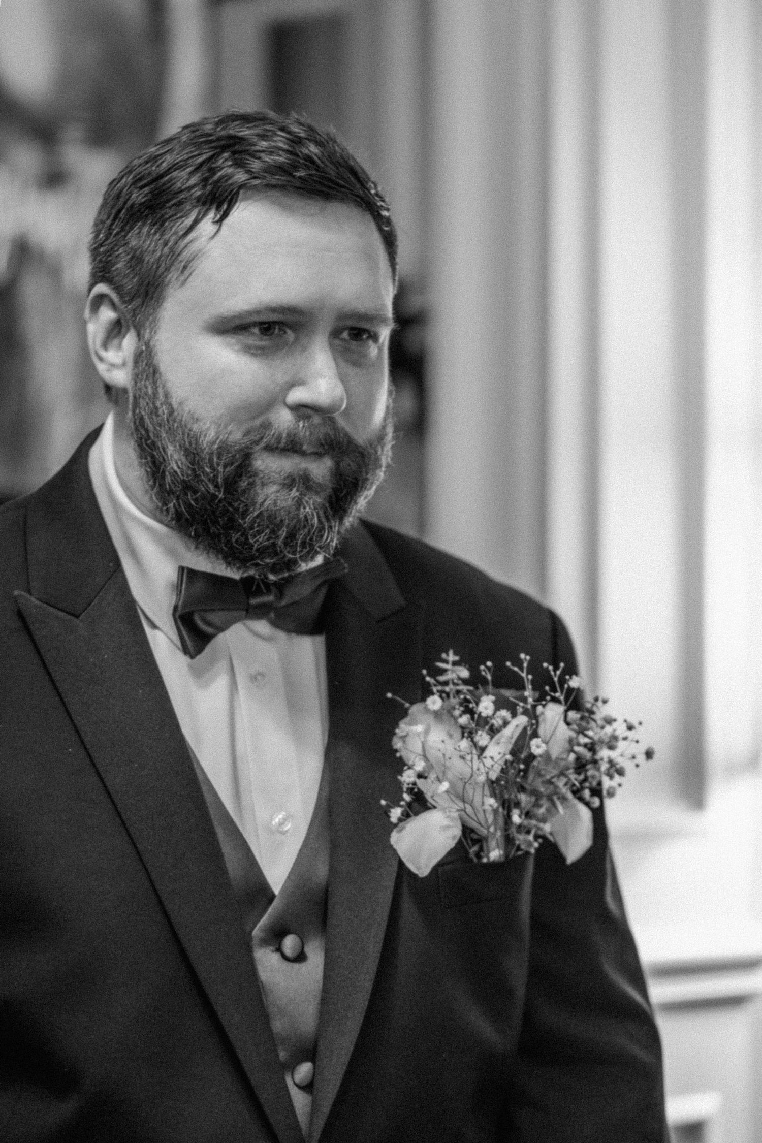 Wedding guest in formal attire with boutonniere smiles during ceremony.