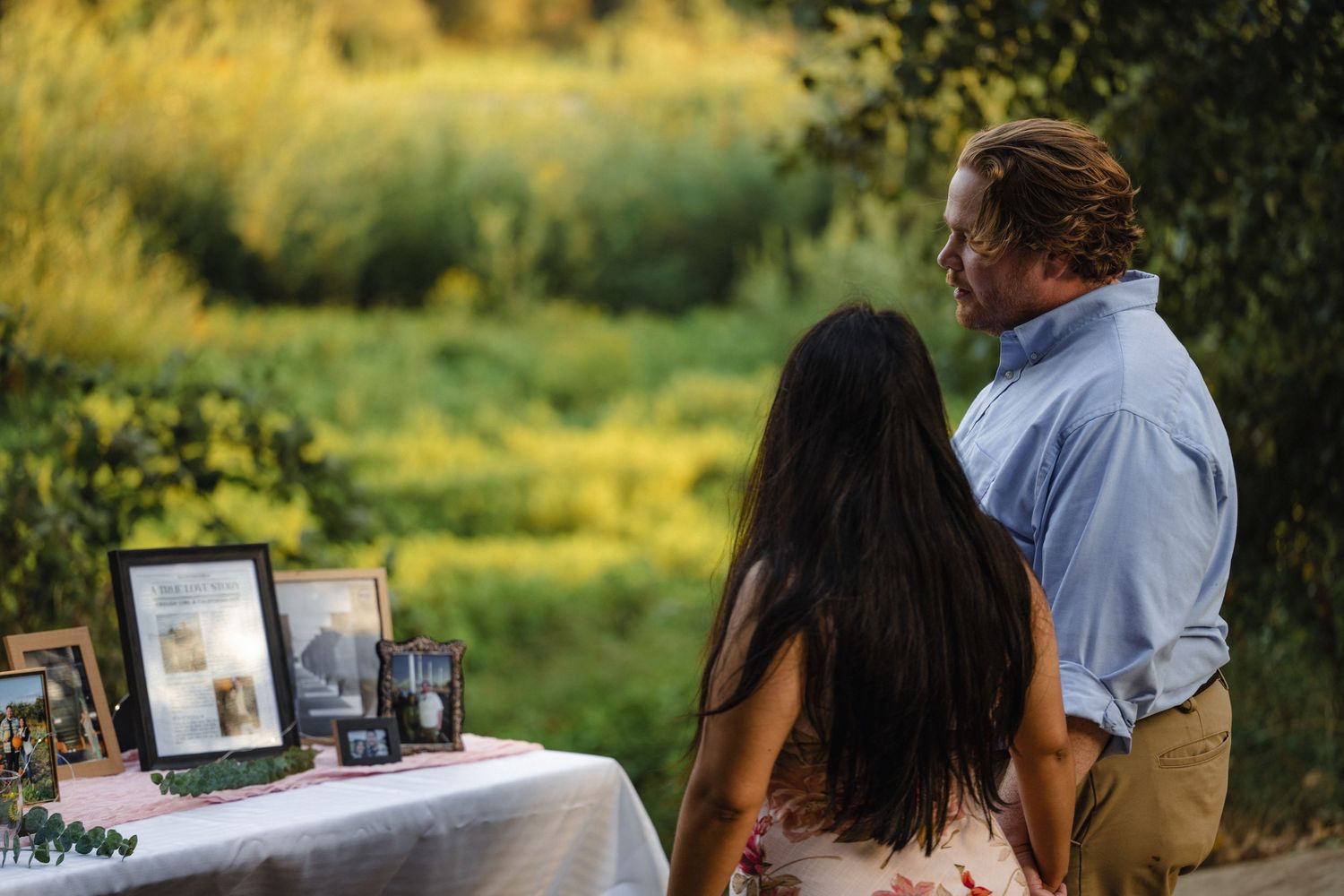 A decorated table with white linens and photo frames set up outdoors for a special occasion.