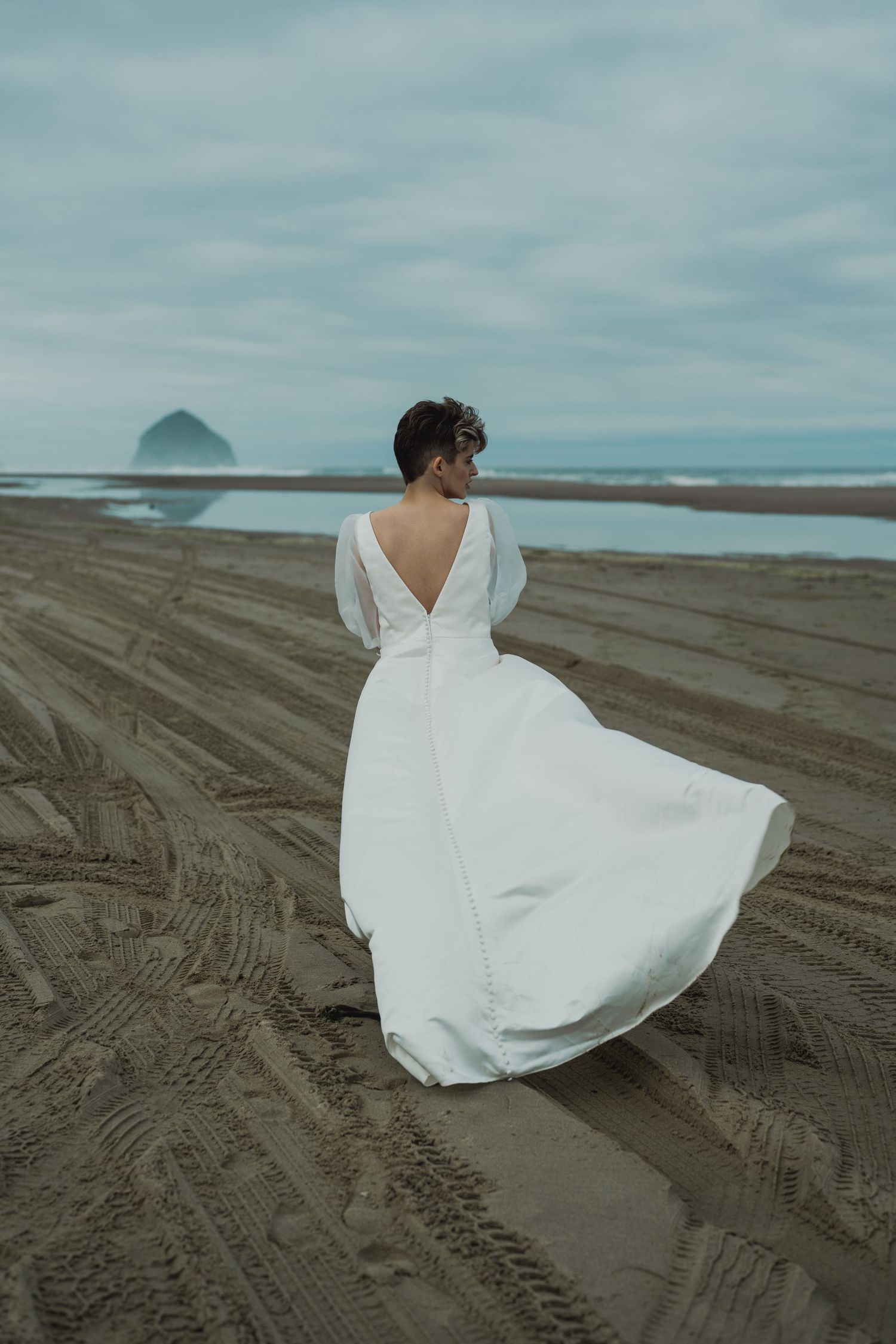 White wedding dress billowing on cloudy beach with ocean view.