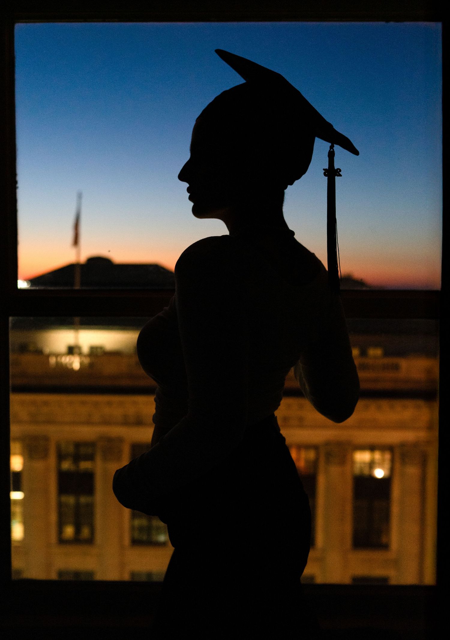 Silhouette of person in graduation cap against sunset sky.