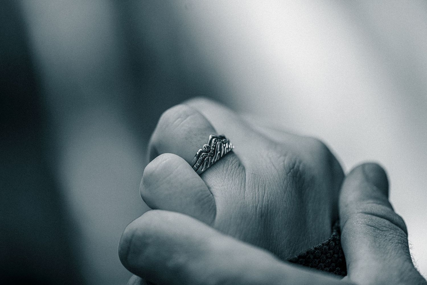 Close-up of a hand wearing an ornate silver wing ring, captured in moody black and white photography.